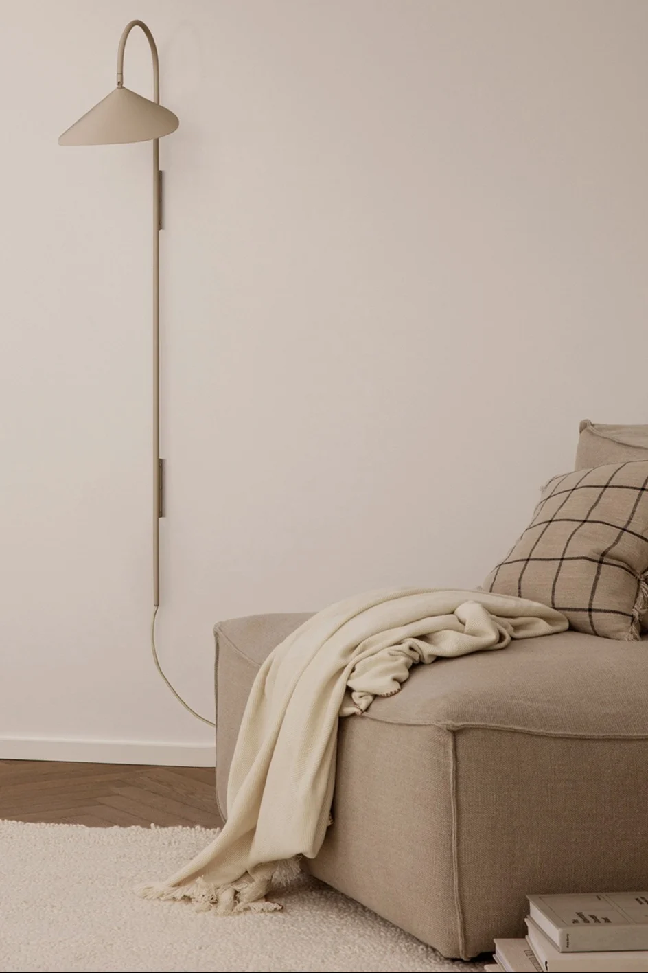 Ein beiges Wohnzimmer mit der beigefarbenen Arum Wandlampe von Ferm Living und einem gemütlichen Loungesessel.