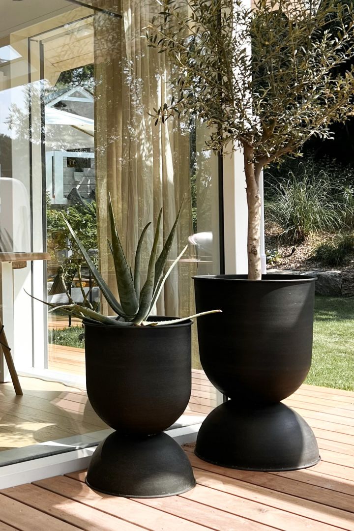 Blumentöpfe für draußen: Hier sehen Sie zwei der großen Outdoor-Pflanzkübel Hourglass von Ferm Living auf einer Terrasse stehen.