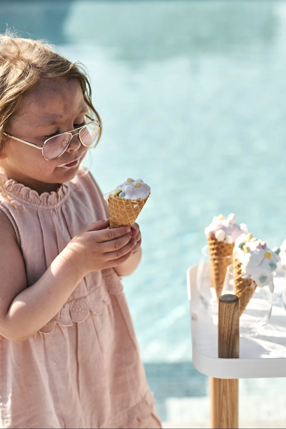 Eis selber machen sollte unbedingt auf Ihrer Summer Bucket List stehen. Hier sehen Sie ein Kind, das ein Eis aus einer Waffel neben einem Pool isst.