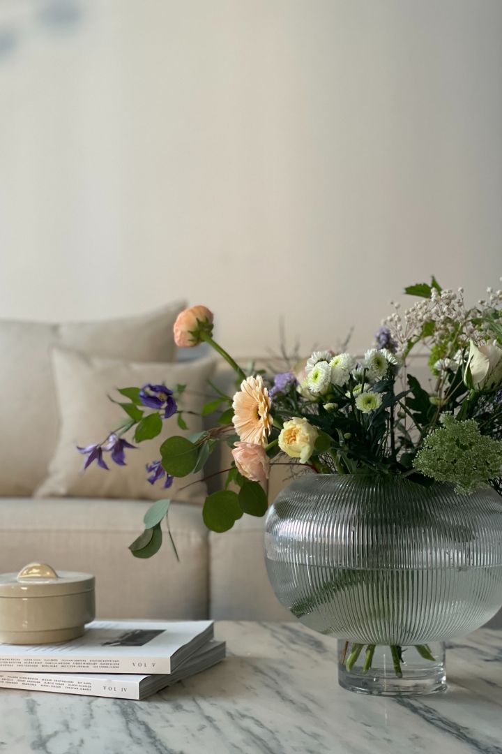 Eine runde durchsichtige Vase mit Blumen auf einem Marmortisch.