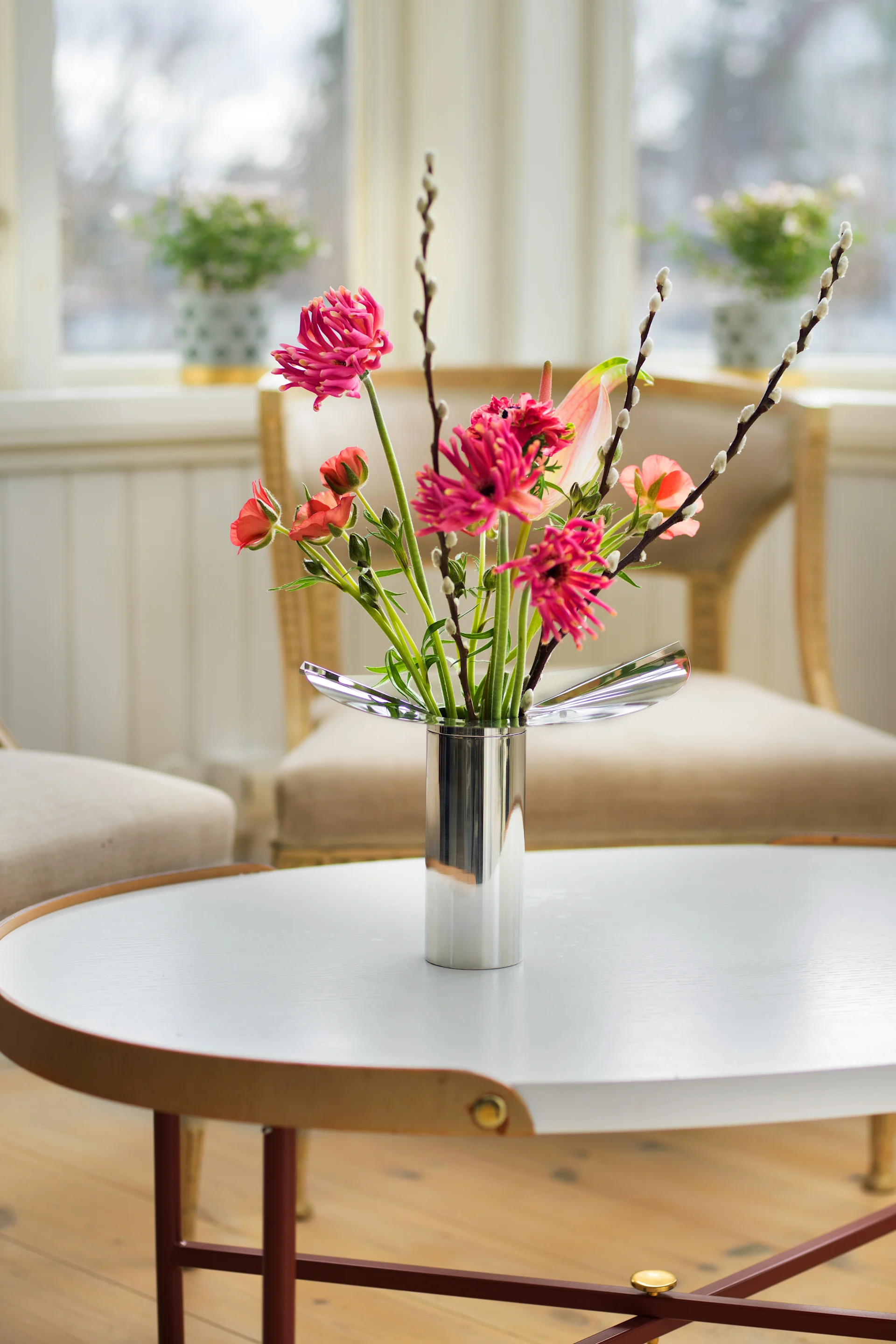 Ein runder Couchtisch ist dekoriert mit der chromfarbenen Löv Vase/ Kerzenhalter von Klong mit frühlingshaften Blumen darin.