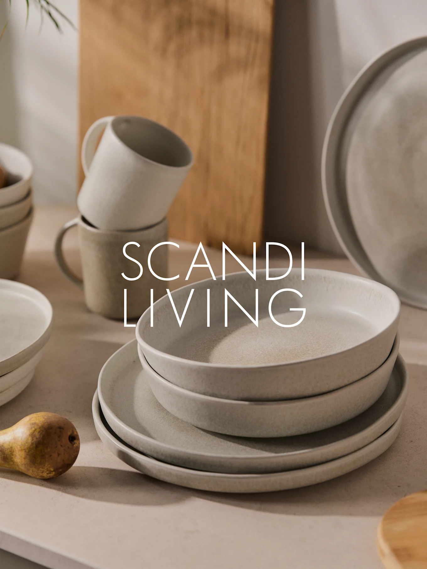 Stapel heller, gesprenkelter Keramikteller, Schalen und Tassen mit einer Birne. Text: SCANDI LIVING.