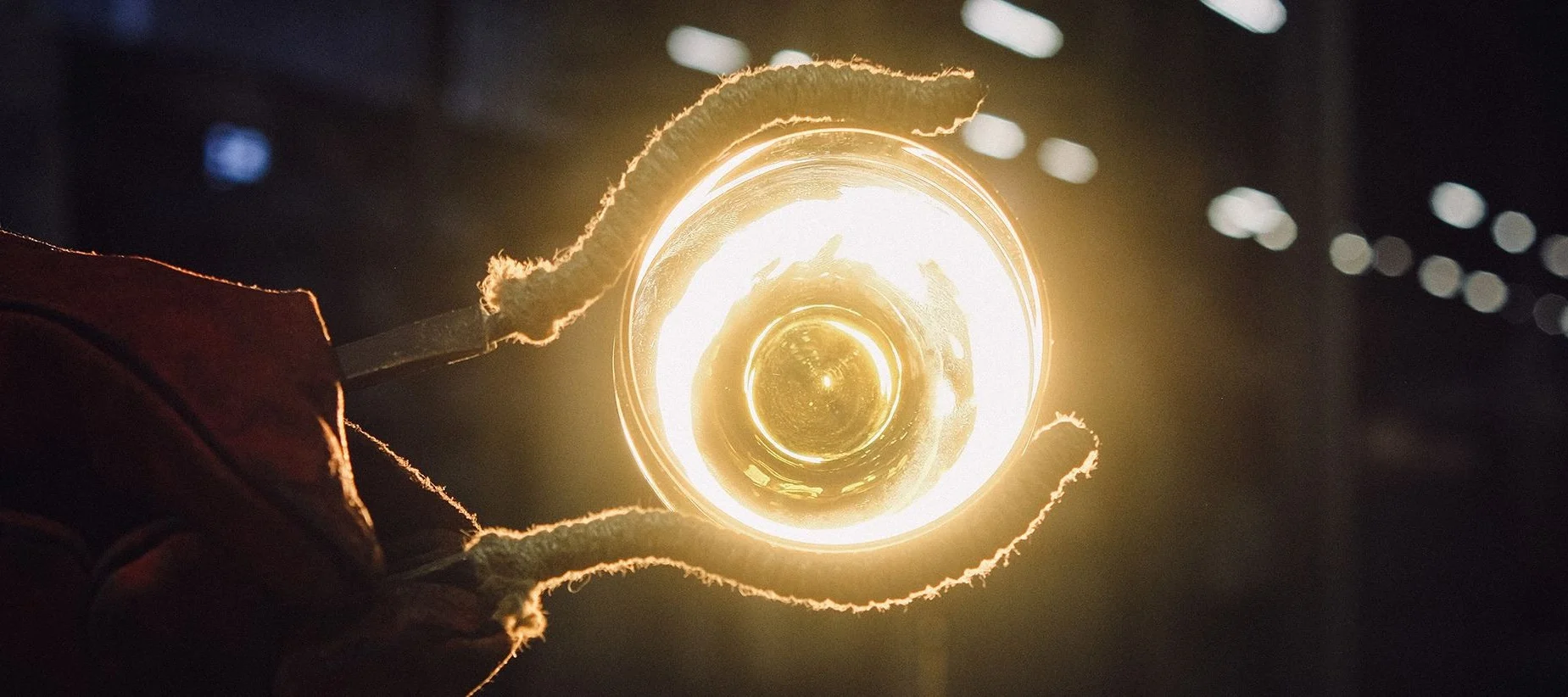 Eine Zange hält ein leuchtendes Glaskunstwerk in der Glashütte von Iittala in Finnland hoch. 