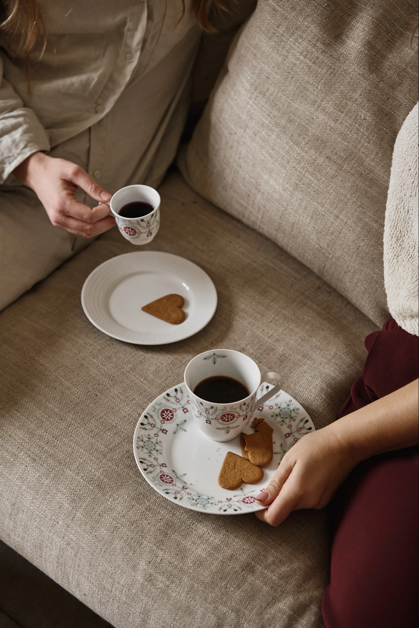 Hier sehen Sie zwei Personen auf einem Sofa sitzen, mit Tassen aus der Swedish Grace Winter-Kollektion von Rörstrand, gefüllt mit Glögg. Die passenden Teller stehen auf dem Sofa und sind mit schwedischen Lebkuchen bestückt.