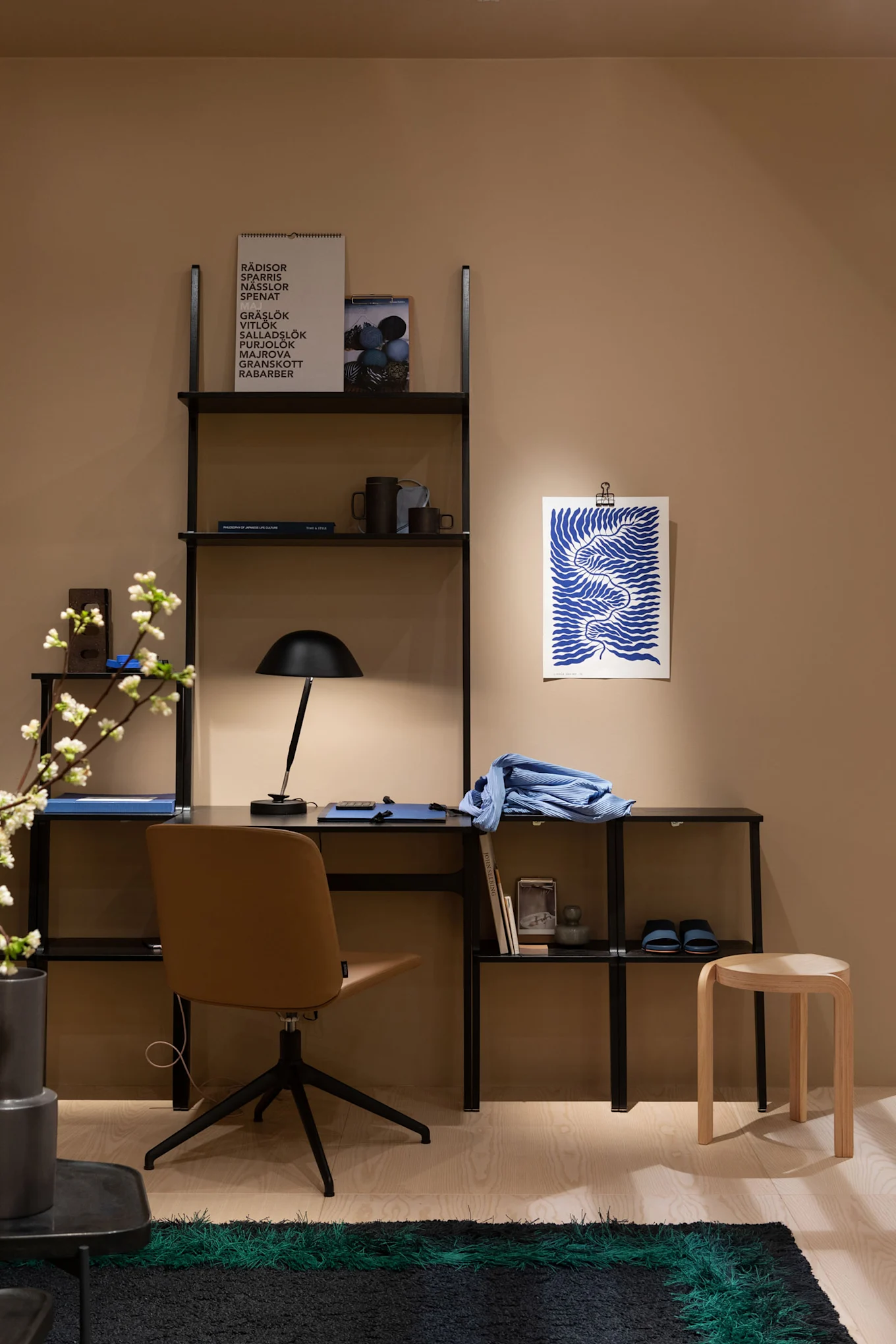 Ein modernes Heimbüro mit schwarzem Regal, braunem Drehstuhl, schwarzer Schreibtischlampe, blauer Kunst und einem grün gestreiften Teppich.