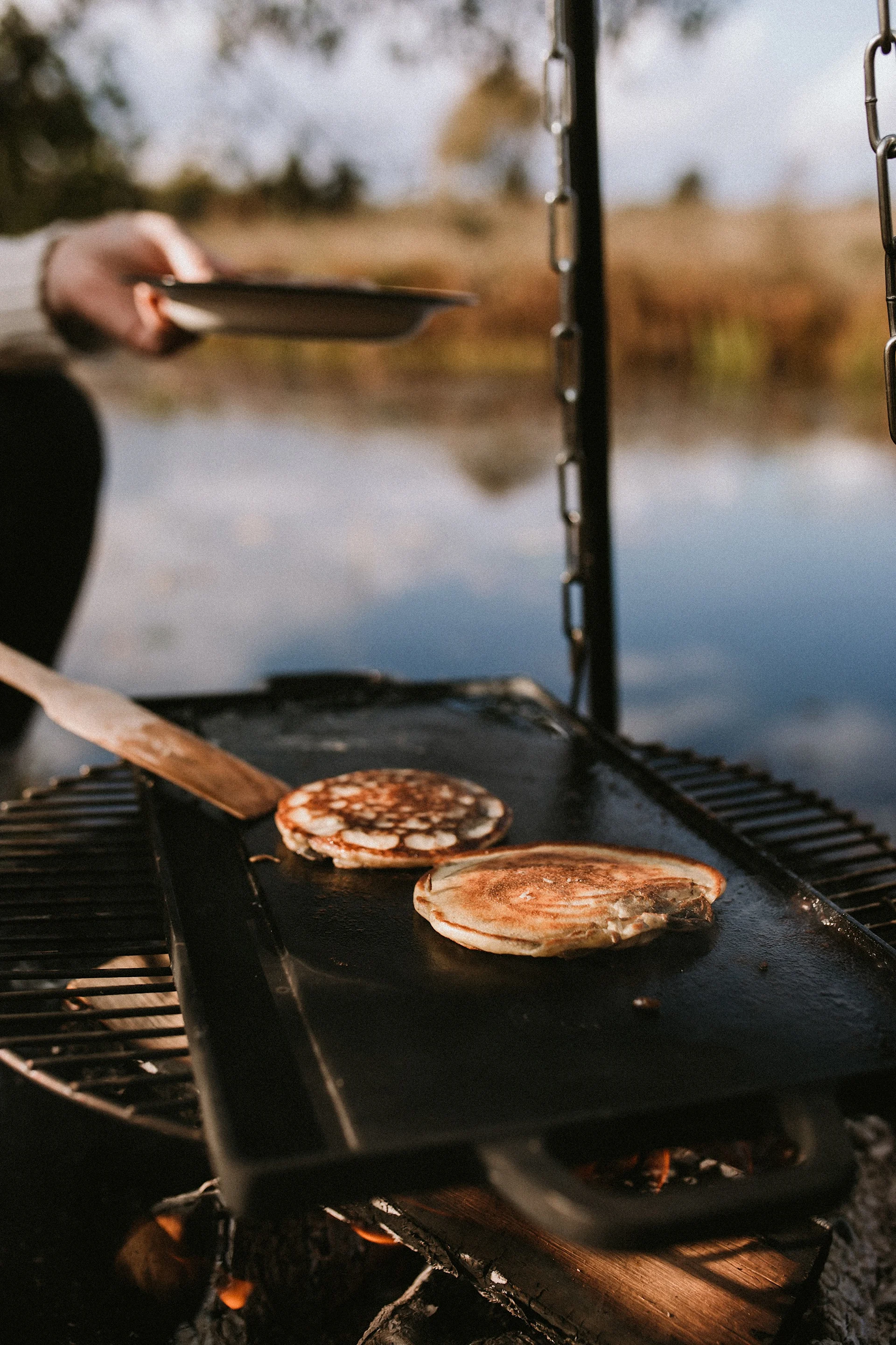 Draußen im Garten zu kochen liegt 2025 im Trend - zum Beispiel auf offenem Feuer, mit dem Satake Brattisch, auf dem hier Pfannkuchen gebacken werden.