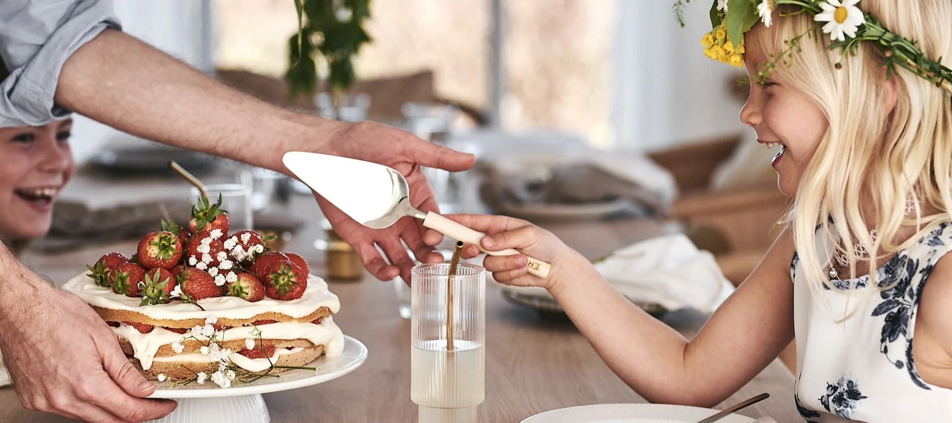 Midsommar in Schweden: Ein Kind schneidet einen traditionellen Erdbeerkuchen an, während es einen Mittsommerkranz trägt.