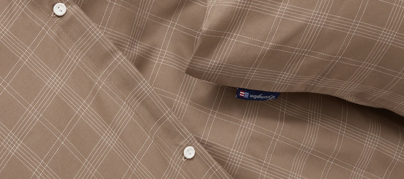 Nahaufnahme eines braunen Stoffes mit weißem Karomuster, mit zwei weißen Knöpfen und einem blauen Lexington-Etikett.
