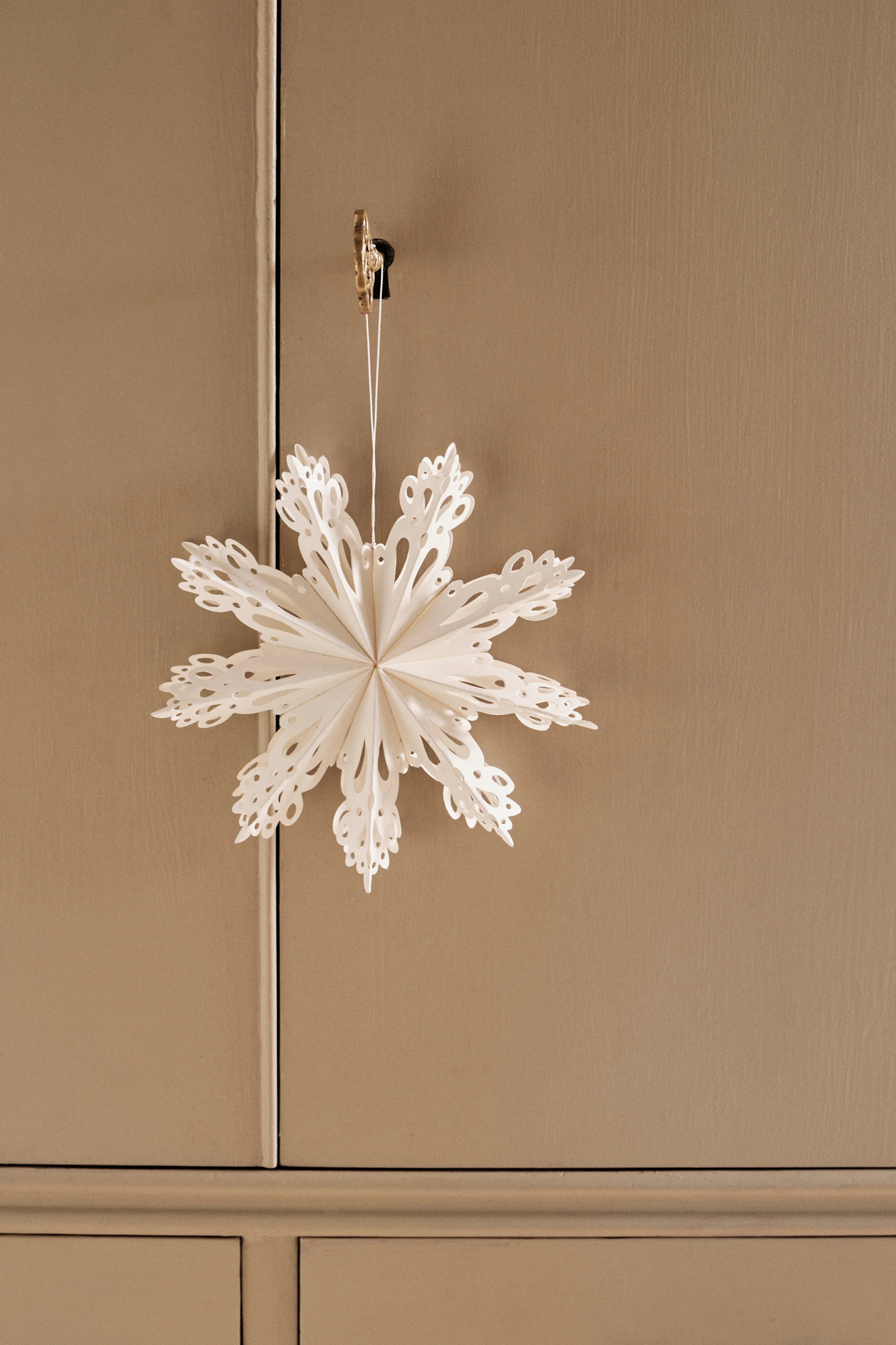 Rustikale Wohndeko mit Konsolentisch, Stuhl, Vase mit grünen Zweigen, gefaltetem Papierstern-Ornament und brennenden Kerzen auf Leinentuch.