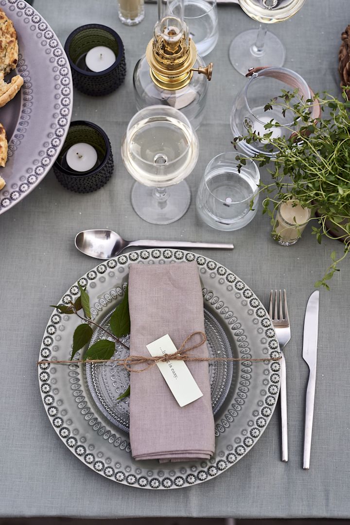 Decken Sie den Tisch für Mittsommer in grünen Farben mit rustikalem Porzellan von Potteryjo, grüner Tischdecke und Leinenserviette mit einem grünen Zweig. 