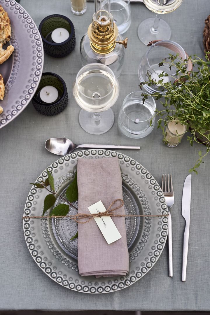 Decken Sie den Tisch für Mittsommer in grünen Farben mit rustikalem Porzellan von Potteryjo, grüner Tischdecke und Leinenserviette mit einem grünen Zweig. 
