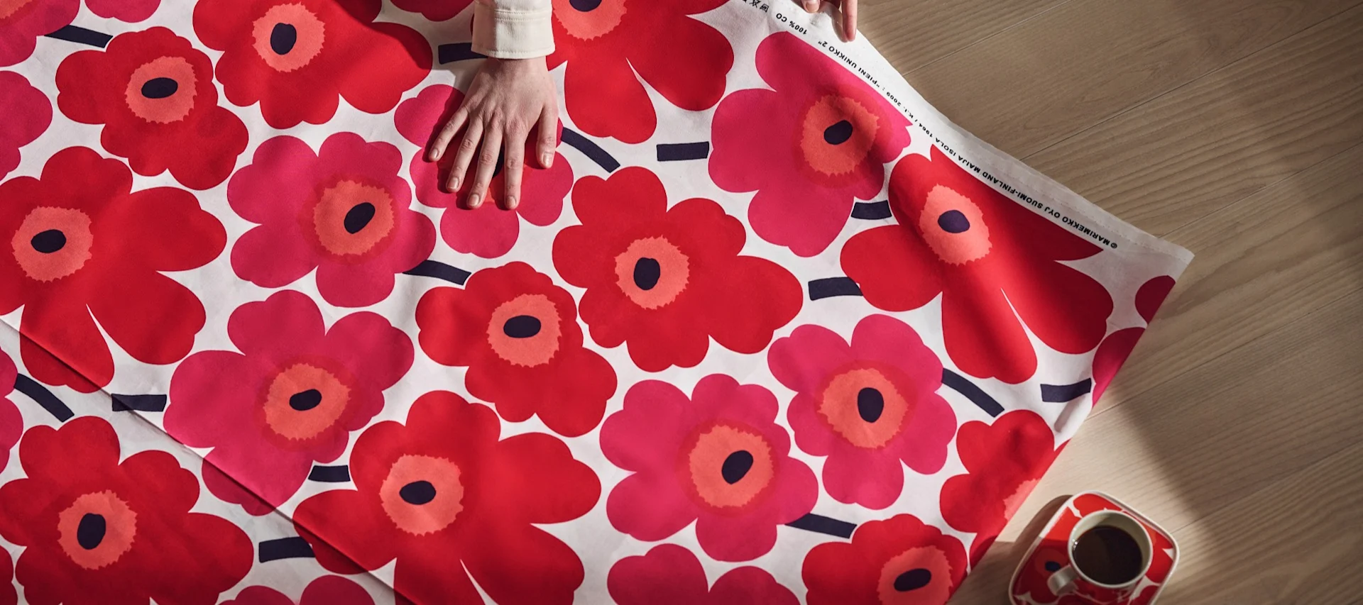 Eine Hand ruht auf einem leuchtend roten Blatt Unikko-Stoff von Marimekko.