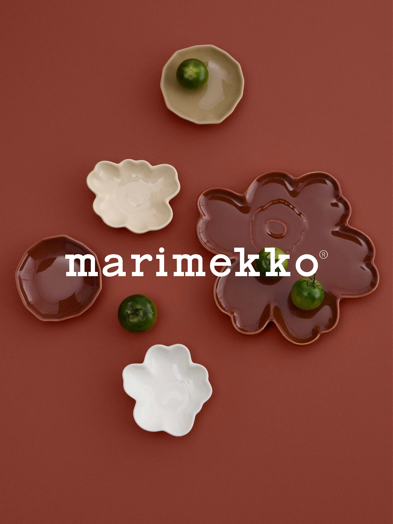 Weißes 'marimekko' Logo, blumenförmige Schalen (weiß, creme, rotbraun) mit grünen Früchten, auf roter Oberfläche.