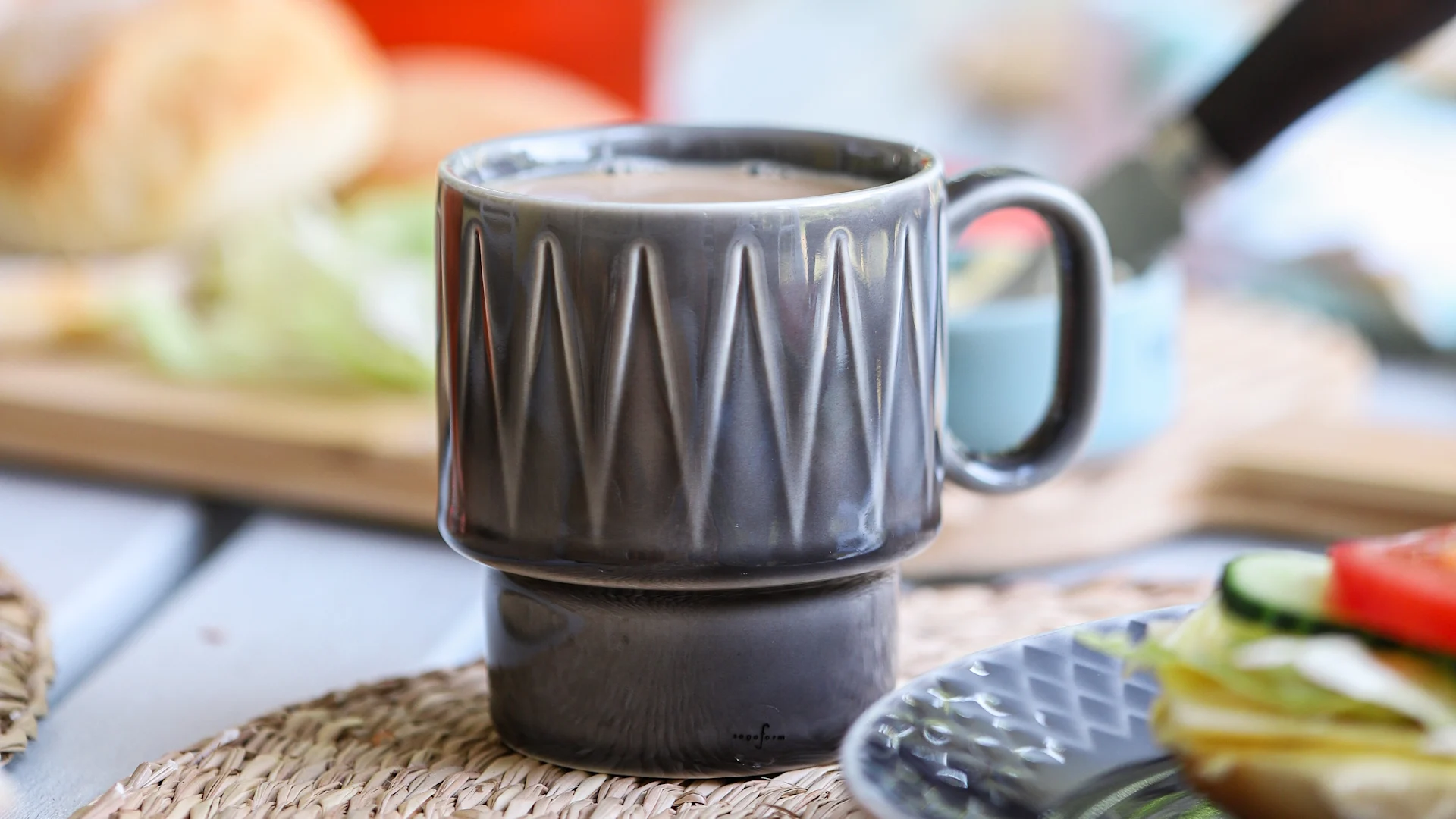 Das Bild zeigt den Coffee Moore Kaffeebecher in Grau von Sagaform, gefüllt mit Kaffee, neben einem Teller mit frisch gebackenen Brötchen.