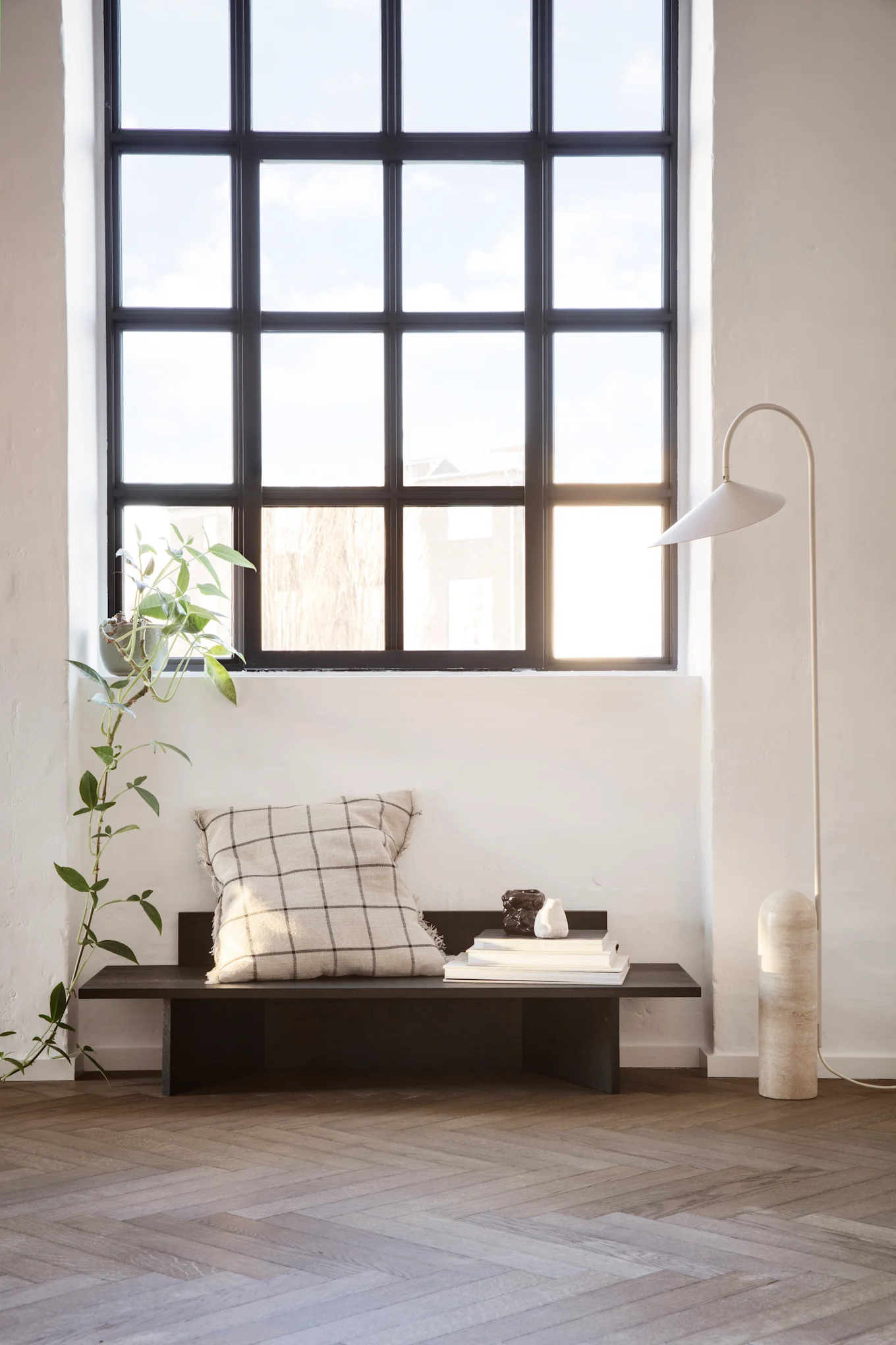 Japandi: Der Japandi-Wohnstil ist hell und freundlich, geprägt von jeder Menge Holz. Hier sehen Sie eine Holzbank, dekoriert mit Kissen und der Arum Stehleuchte von ferm LIVING daneben.