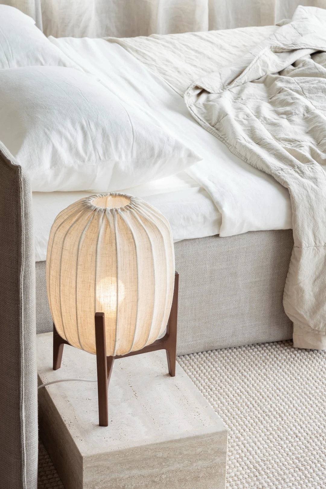 Möbel und Accessoires aus natürlichen Materialien wie Stoff und Holz eignen sich perfekt für einen Lagom-inspirierten Stil. Hier sehen Sie die Prisma Tischlampe von Watt & Veke neben einem Bett stehen.