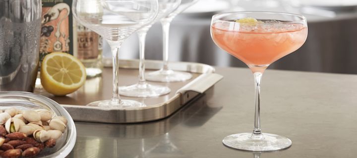 Ein alkoholfreier Cocktail mit Grapefruitsaft im Cabernet Cocktailglas von Holmegaard steht auf einer Küchentheke, im Hintergrund sind Cocktail-Utensilien zu sehen.