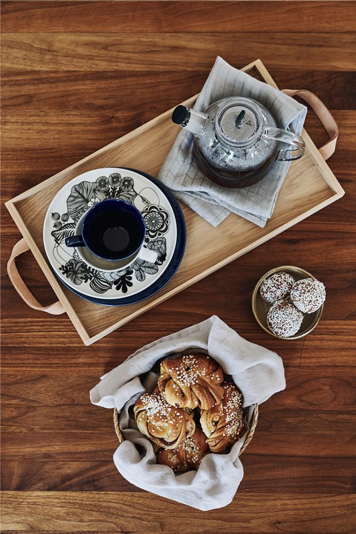 Eine klassische schwedische Fika wird in der Küche auf einem Holztablett mit Kaffee, Zimtschnecken und Schokoladenkugeln serviert. 