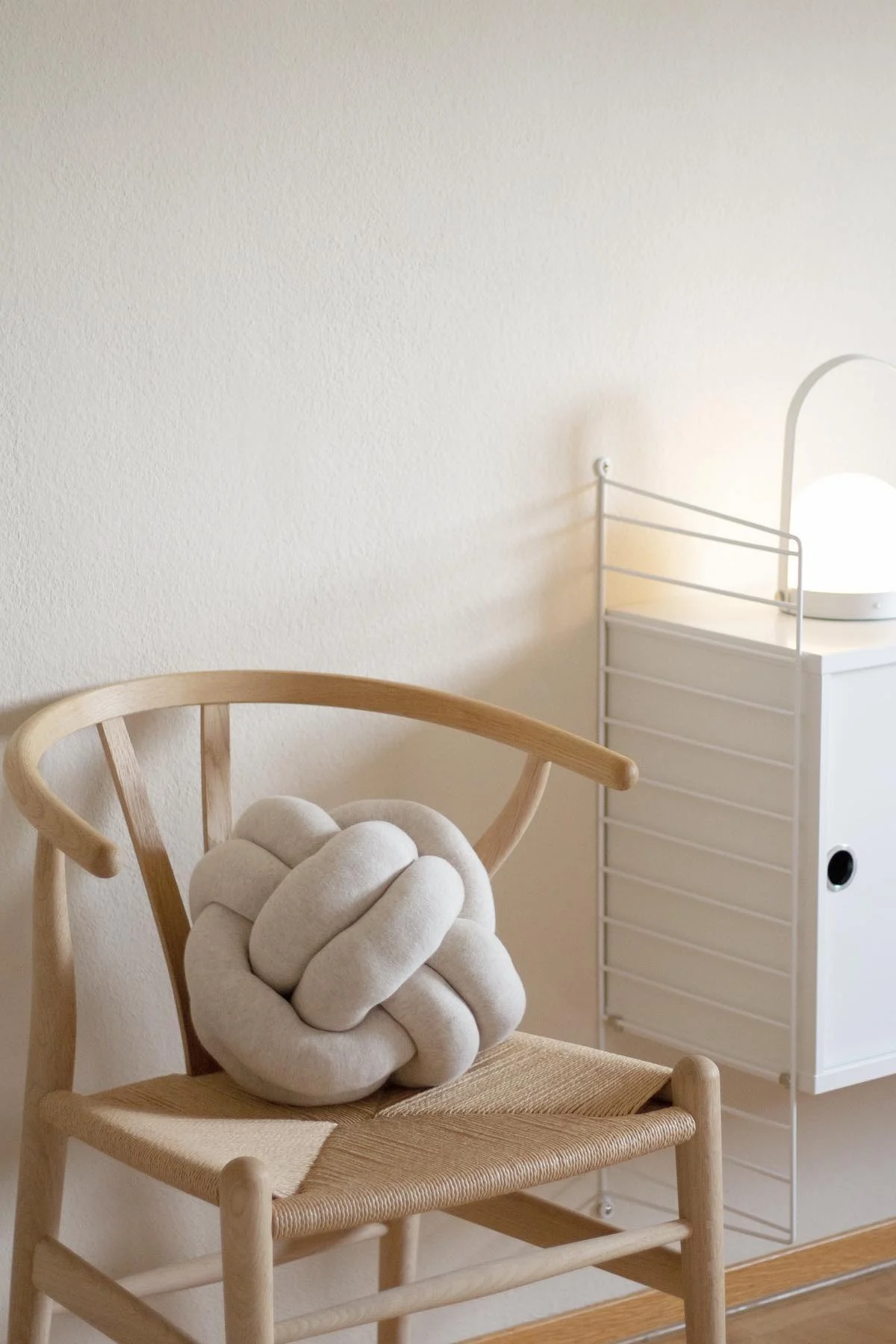 Das beigefarbene Knot Kissen von Design House Stockholm liegt auf dem CH24 Y-Stuhl von Carl Hansen im beigen Wohnzimmer von @b.wohnbar.