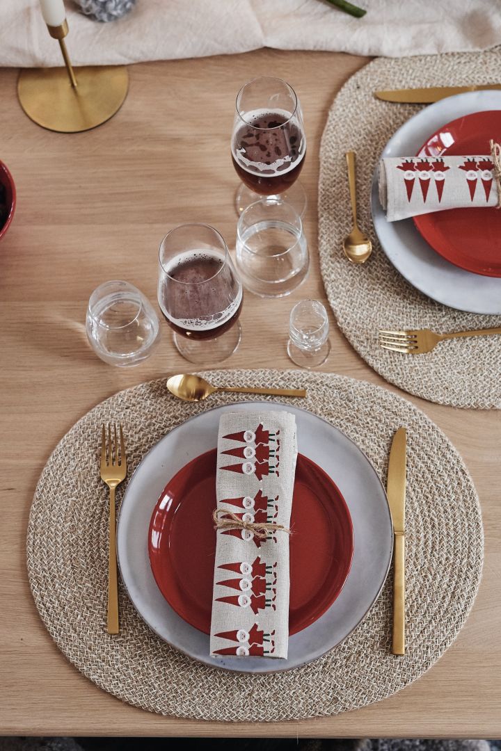 Eine einfache Weihnachtstischdekoration, bei der das Gedeck aus einem blaugrauen Teller, einem roten Teller und goldenem Besteck besteht.