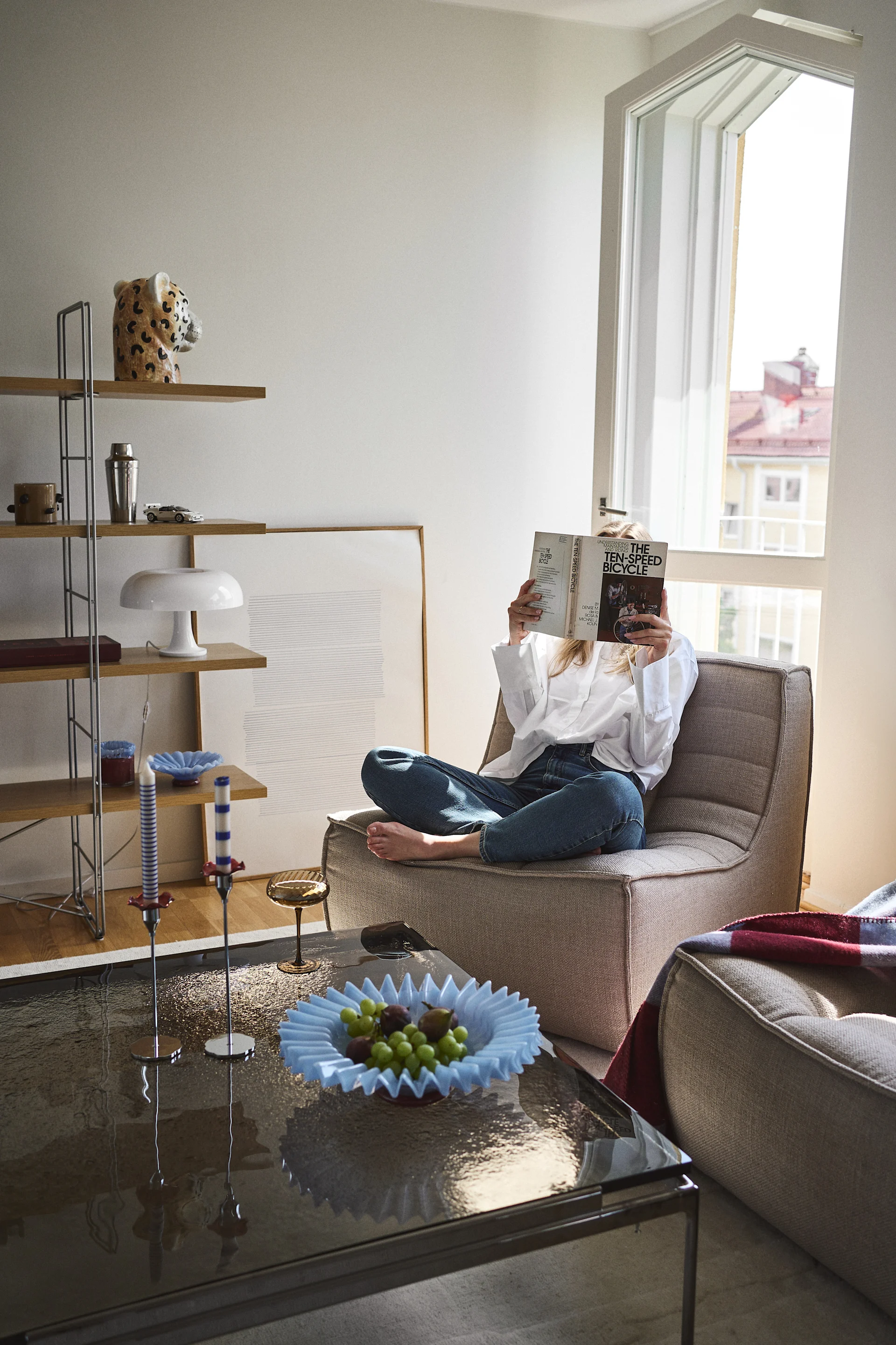 Die Dekoration des Wohnzimmers mit Statement-Stücken von Byon schafft ein persönliches und eklektisches Zuhause, das mit Freude, Form und Farbe gefüllt ist. Hier die Schale Lori in Hellblau, die Vase Cheetah, das Champagnerglas Opacity, die Decke Embrace und das Windlicht Lara.