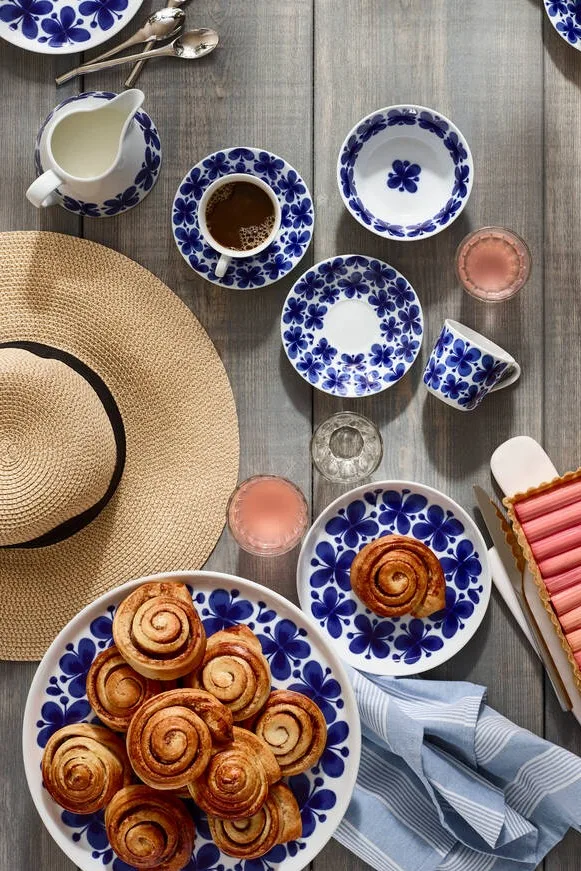 Schwedische Zimtschnecken sind das bekannteste Fika-Gebäck, auch über die Grenzen von Schweden hinaus. Hier sehen Sie sie auf dem Mon Ami-Geschirr von Rörstrand auf einem Tisch im Freien mit einem Sommerhut angerichtet.