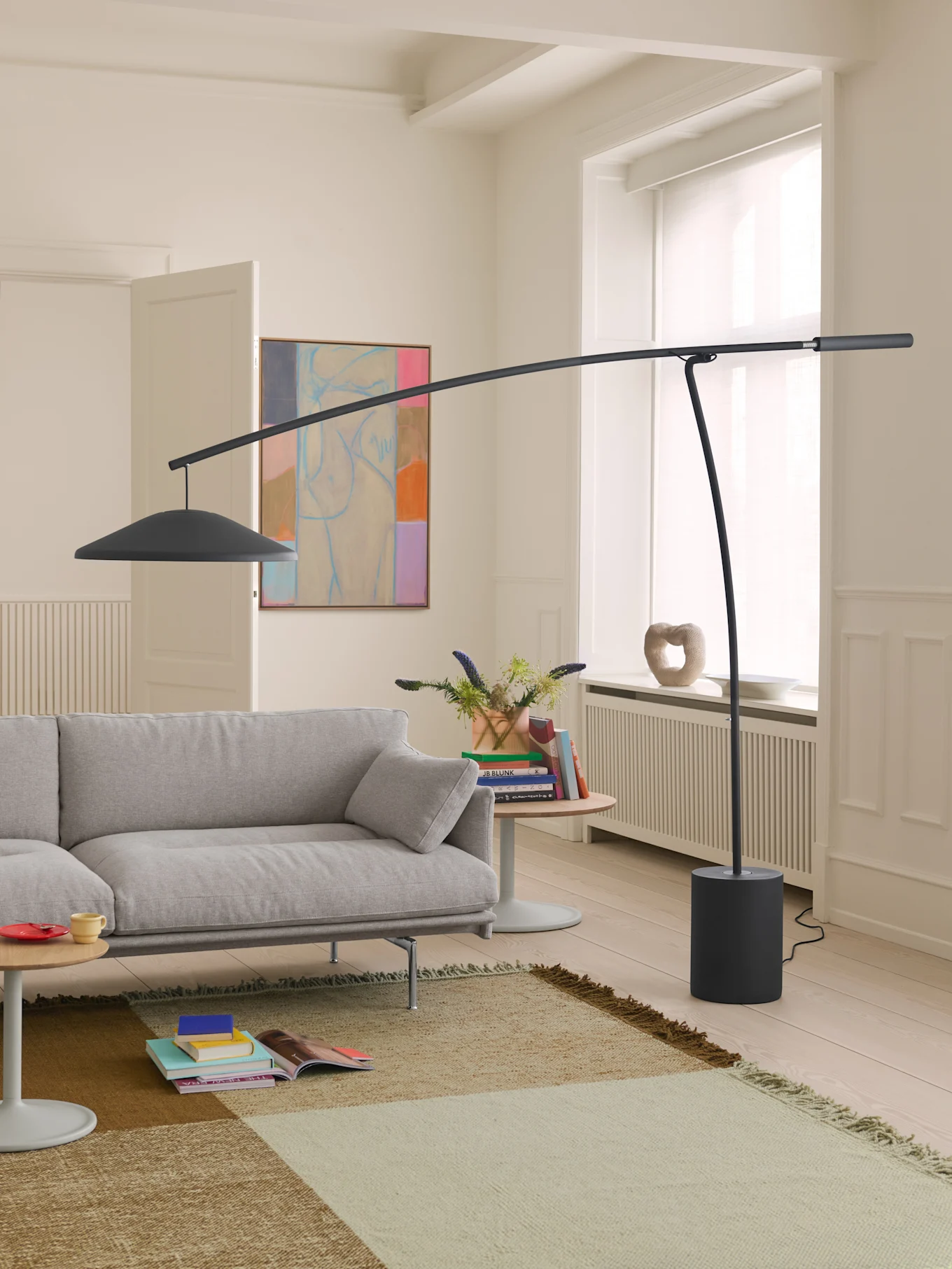 Ein modernes Wohnzimmer mit hellgrauem Sofa, großer dunkelgrauer Bogenlampe und gemustertem Teppich auf hellem Holzboden.