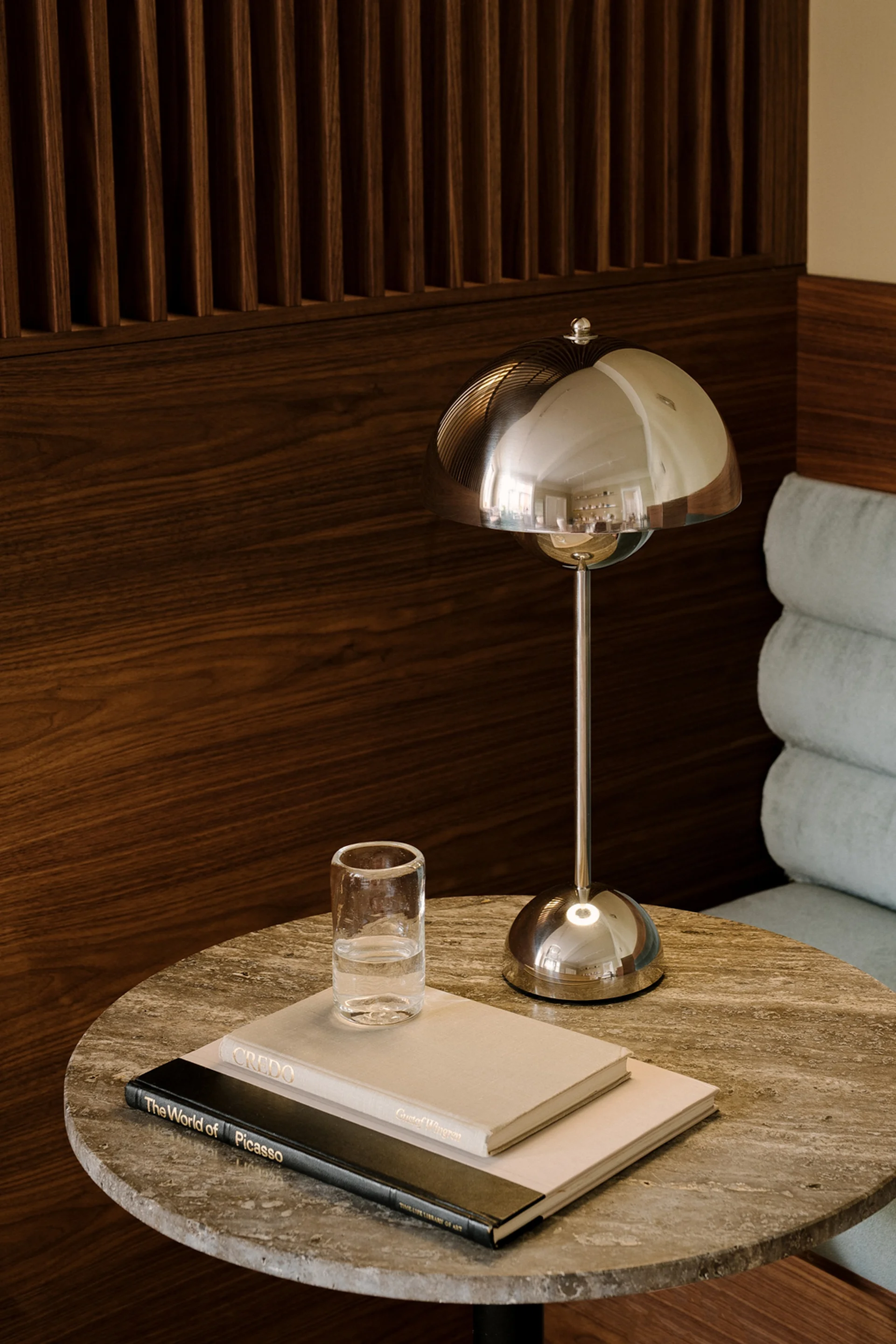 Eine polierte Chrom-Pilz-Tischlampe, ein Glas Wasser und zwei Bücher auf einem runden Marmortisch.