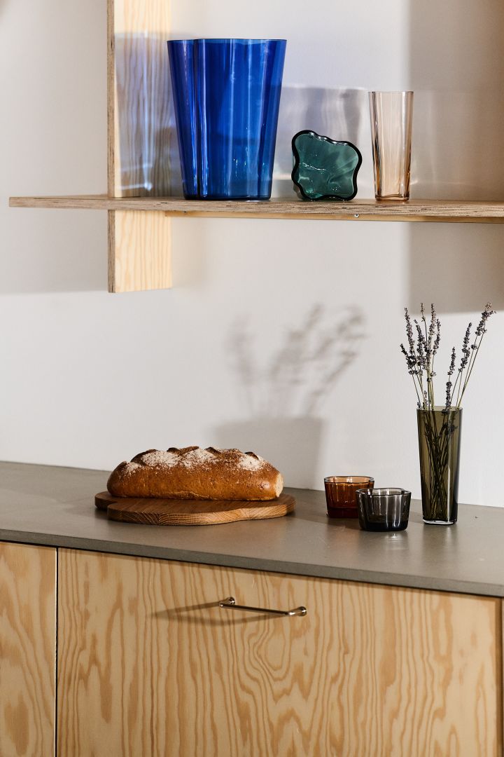 Hier sehen Sie Vasen und Kerzenhalter aus der Alvar Aalto-Kollektion von Iittala auf einem Holzregal und einem Küchenschrank.