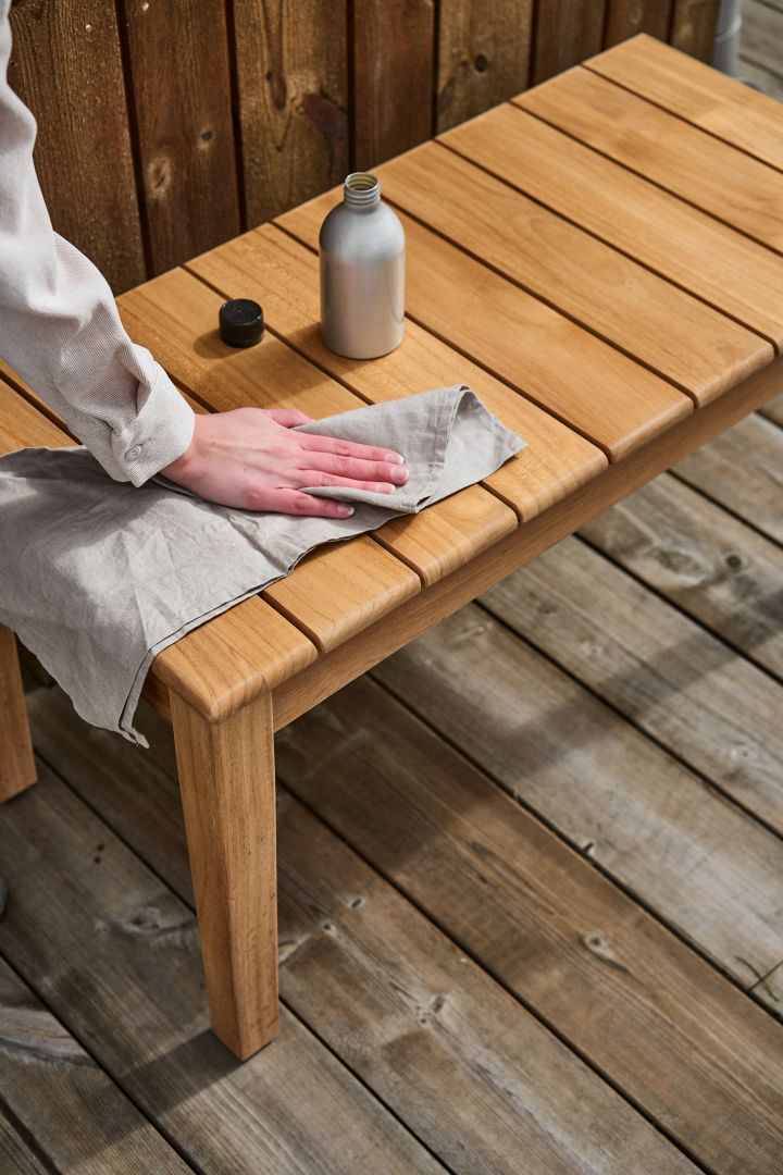 Gartenmöbel aus Teak pflegen: Ein Paar Hände trägt Öl auf ein Tuch auf, um einen Teakholzstuhl mit Teak-Öl zu behandeln.