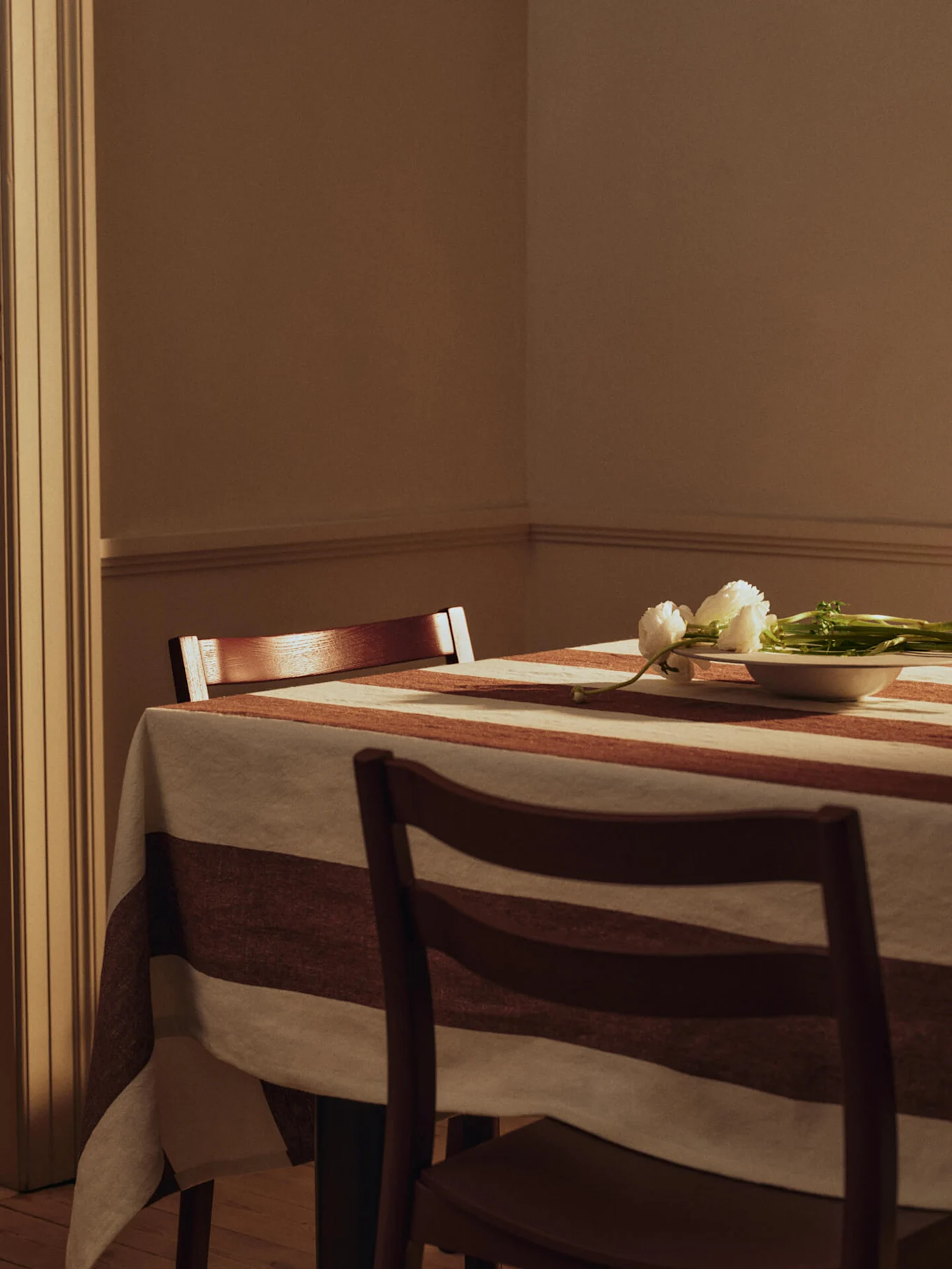 Esstisch mit gestreifter Tischdecke, zwei Holzstühlen und weißen Blumen in einer kleinen Schale.