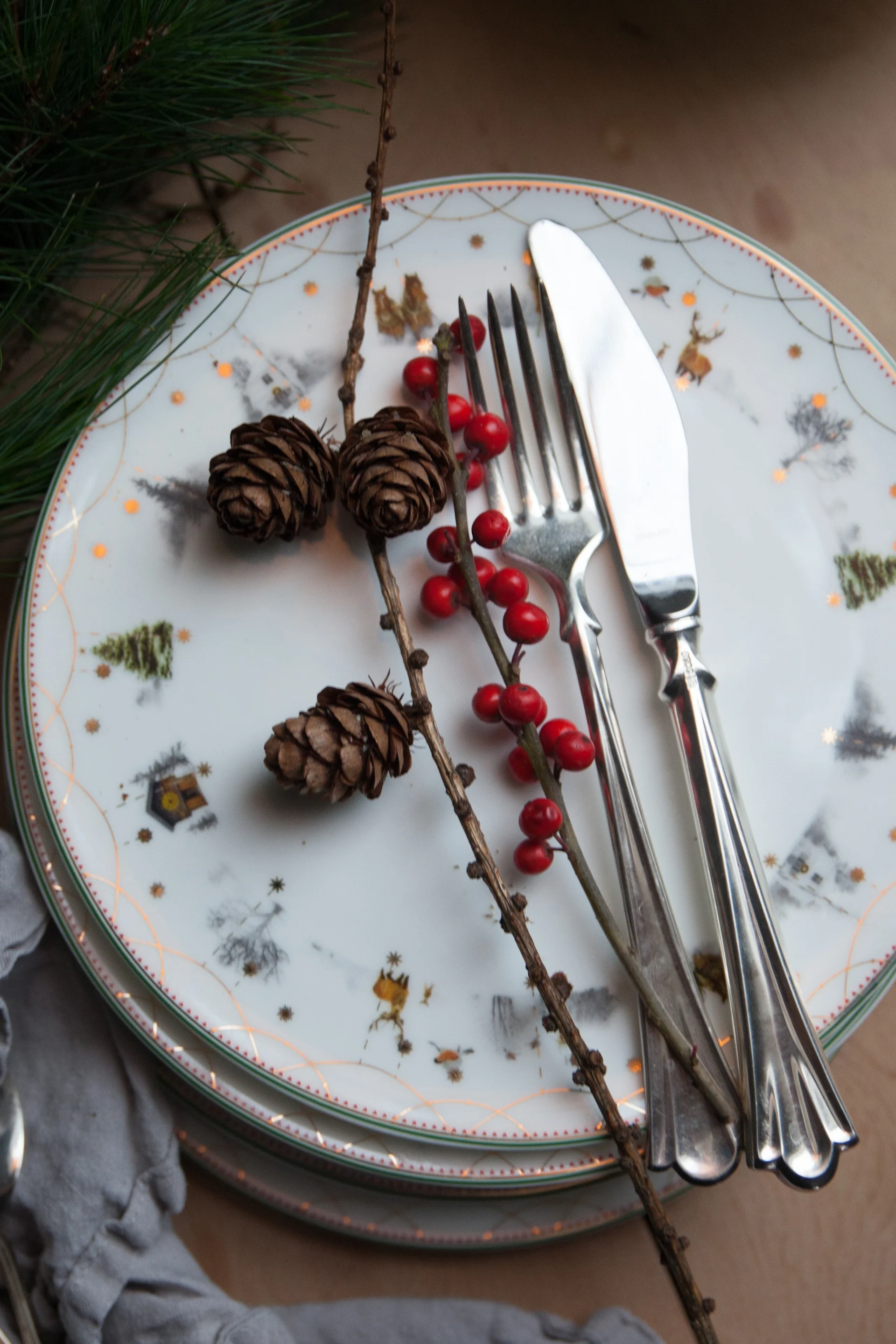Weihnachtliches Geschirr gehört ebenfalls zur skandinavischen Weihnachtsdeko. Hier steht ein Stapel Teller aus der Julemorgen-Kollektion von Wik & Walsøe auf einem Tisch, darauf Besteck.