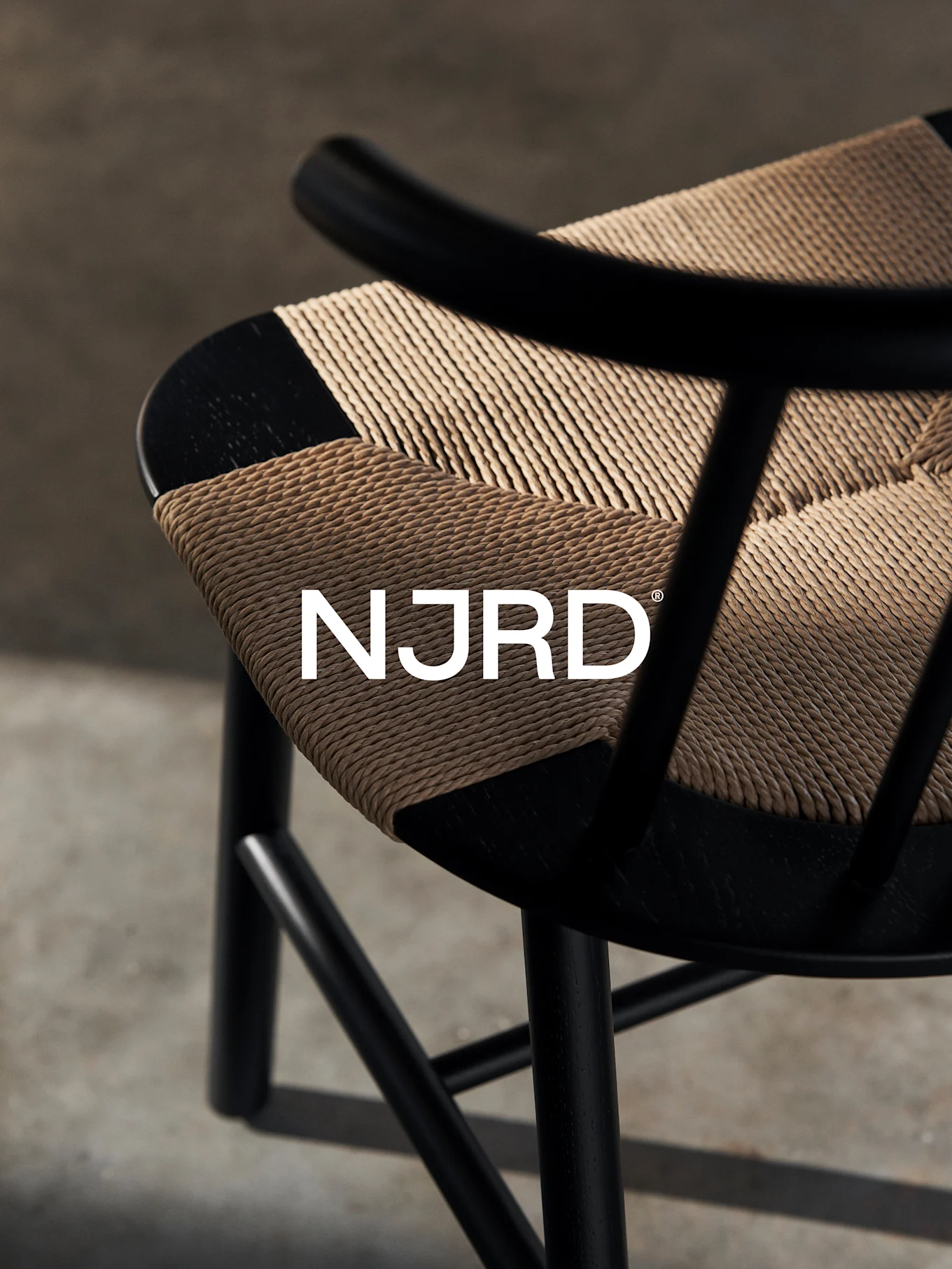Nahaufnahme eines schwarzen Stuhls mit einer gewebten hellbraunen Sitzfläche, mit dem weißen 'NJRD'-Logo.