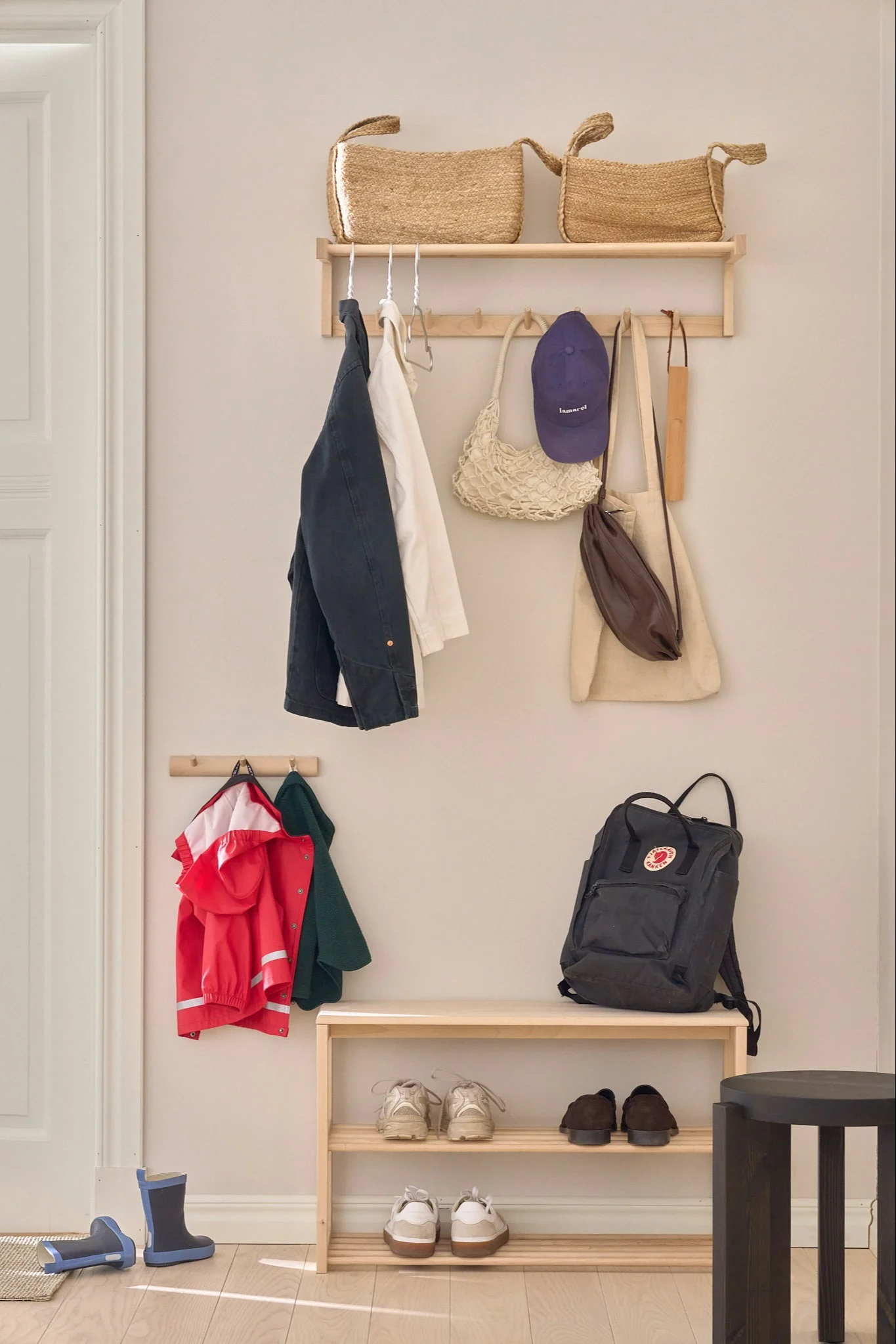 Ein gemütlicher Eingangsbereich mit einem Schuhregal aus Holz, Regalen und Haken für Jacken, Taschen und Schuhe. Blaue Gummistiefel liegen auf dem Boden.