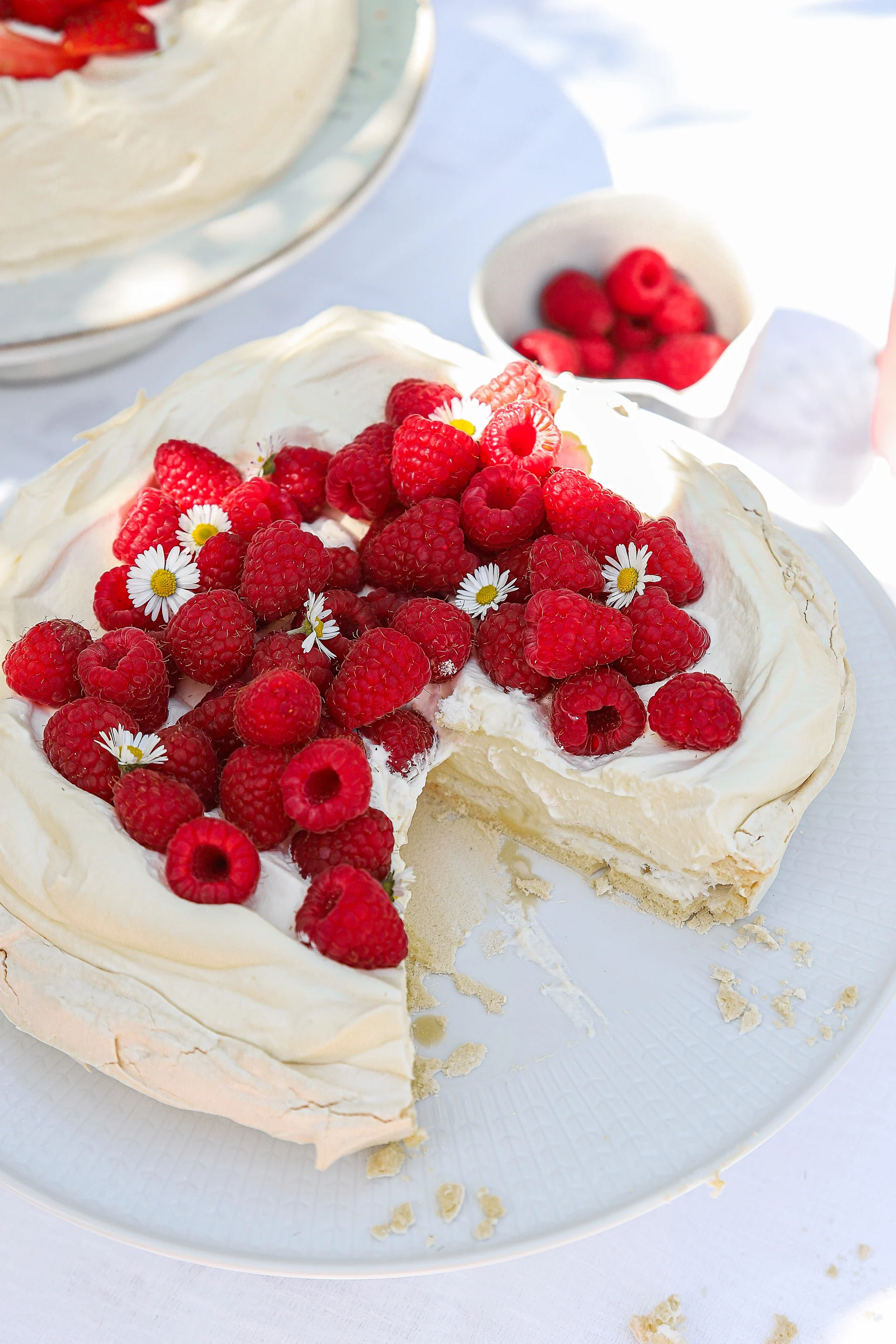 Eine Himbeertorte mit Baiserboden steht auf einem Tortenteller auf einem Tisch.