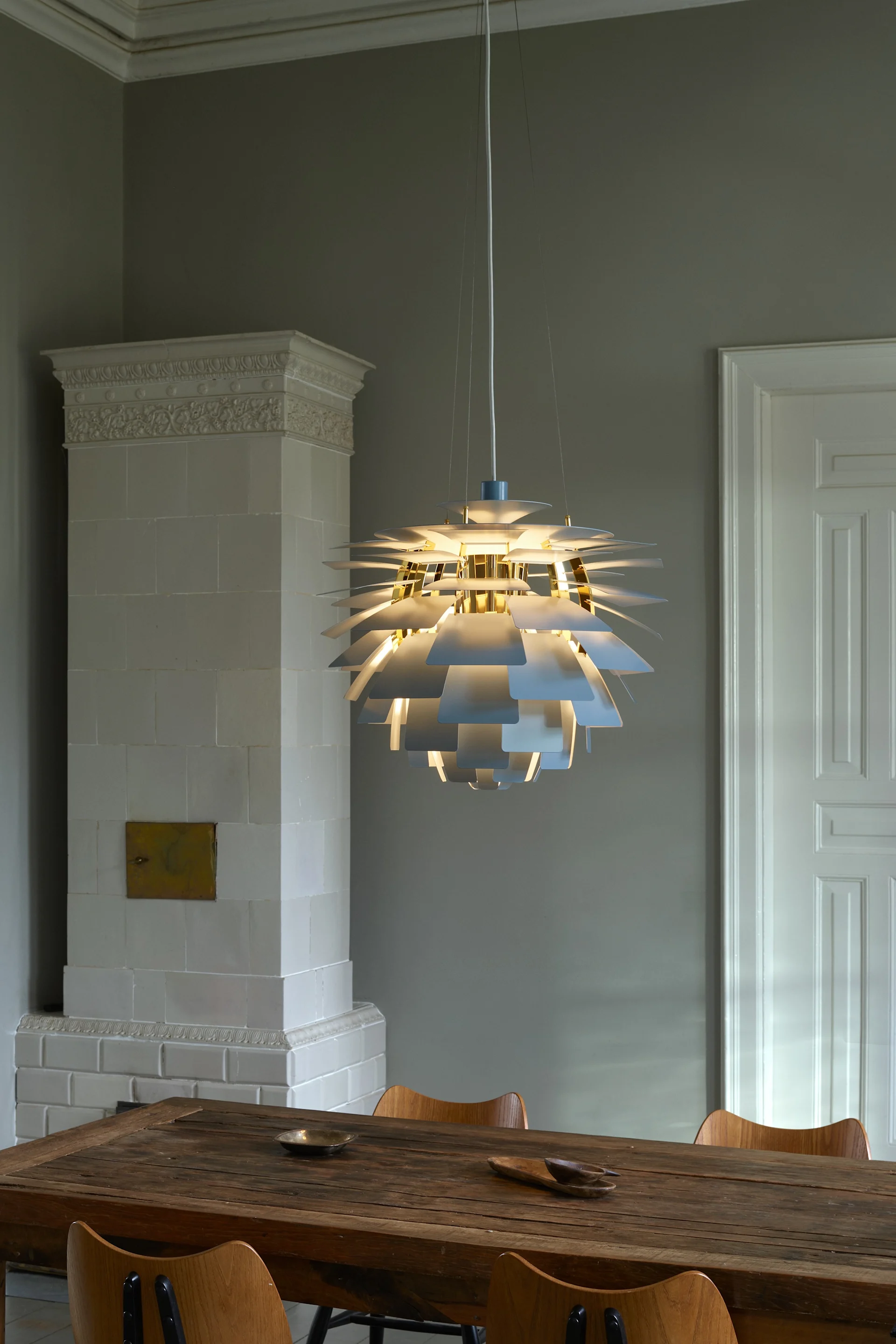 Eine strahlende, mehrschichtige Pendelleuchte mit weißen und goldenen Akzenten, die einen rustikalen Holztisch beleuchtet.