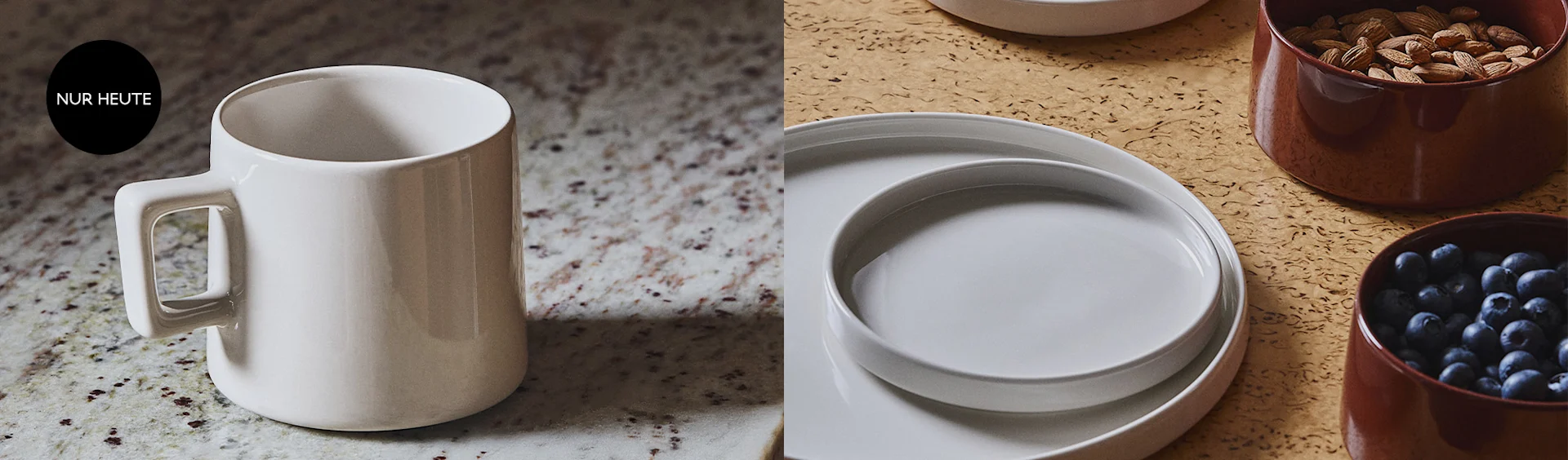 Ein weißer Becher auf einer gesprenkelten Arbeitsplatte mit einem 'NUR HEUTE'-Schild, daneben weiße Teller und braune Schalen gefüllt mit Mandeln und Heidelbeeren auf einem strukturierten, hellbraunen Untergrund.