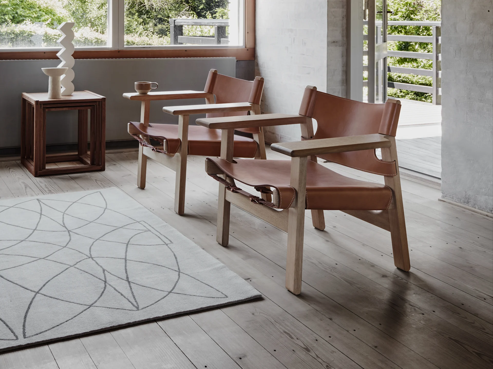 Ein moderner Sessel aus hellem Holz und braunem Leder neben einem runden Holztisch auf einem Betonboden mit Sonnenlicht.