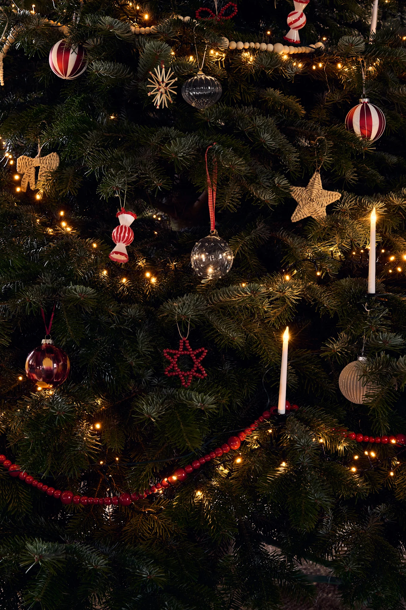 Ein reich geschmückter Weihnachtsbaum mit verschiedenen Ornamenten, warmen Lichterketten und leuchtenden Kerzen.