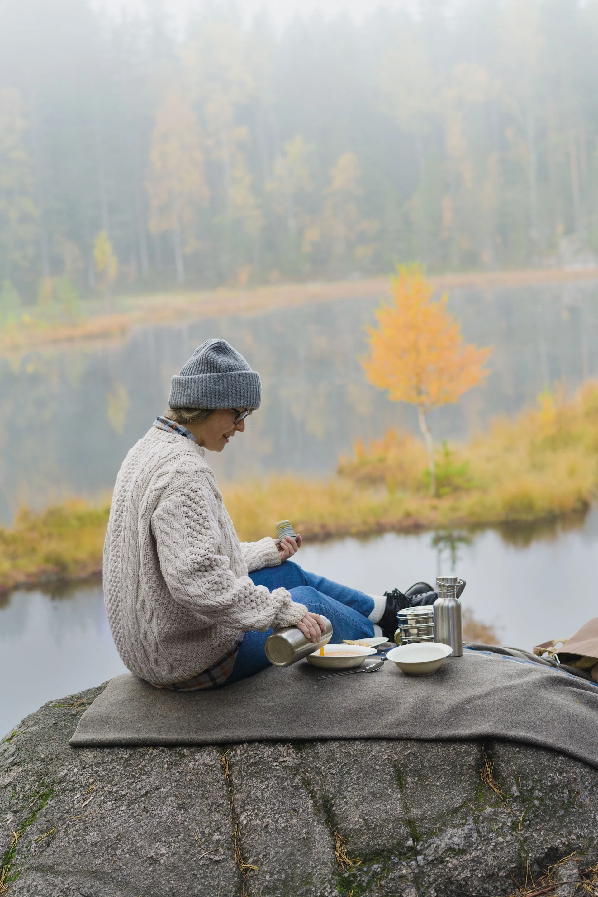Lagom: Eine Frau macht ein Picknick auf einem Berg, rundherum ist eine herbstliche Landschaft zu sehen.