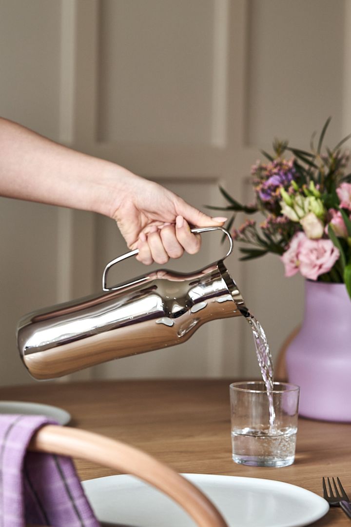 Eine Hand schenkt Wasser aus der Dorotea-Karaffe aus poliertem Edelstahl ein. 