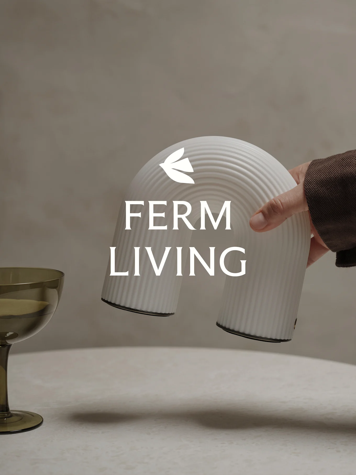 Hand hält ein weißes, geripptes, bogenförmiges Deko-Objekt, mit einem grünen Glas daneben.