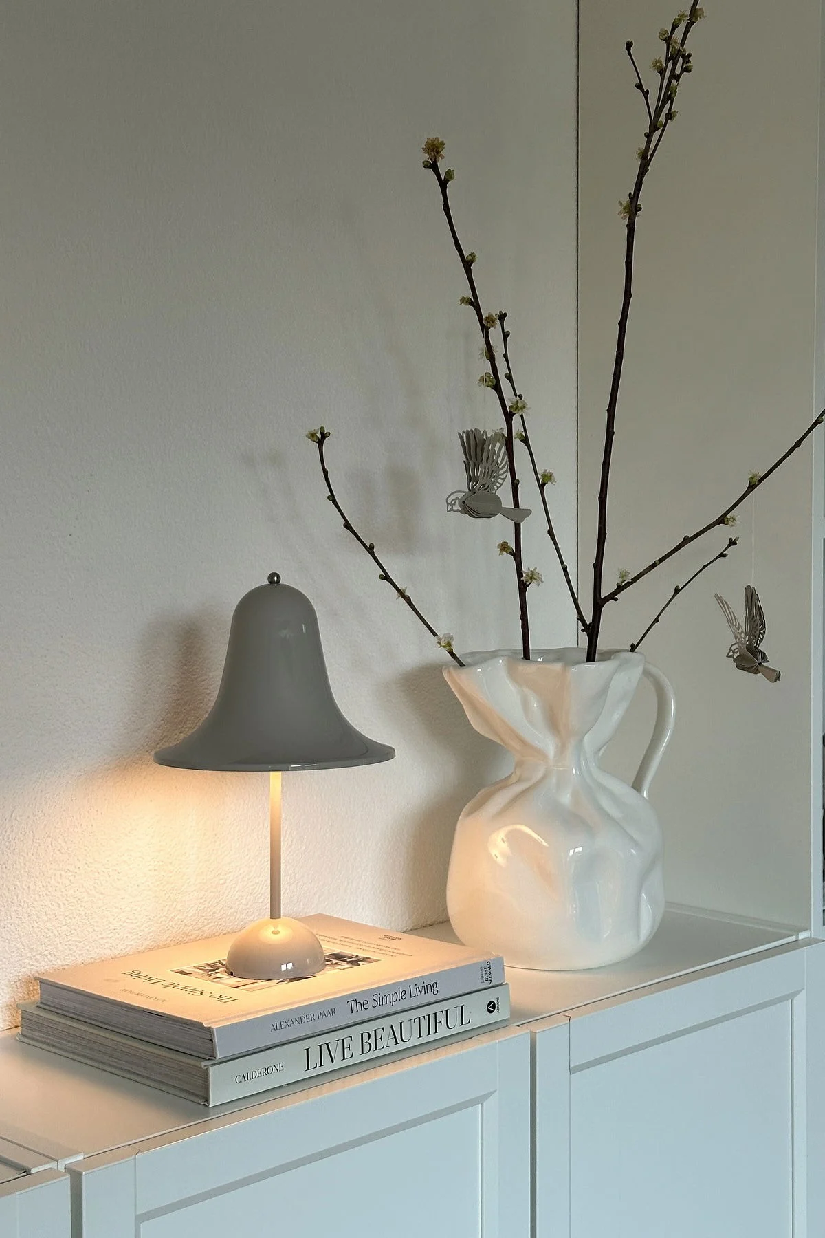 Bei @oursmall.home sehen Sie gleich zwei mögliche Muttertagsgeschenke: Die Pantorp Tischleuchte von Verpan steht auf einer Kommode, daneben die Crumple Vase von Byon mit ein paar Zweigen darin.