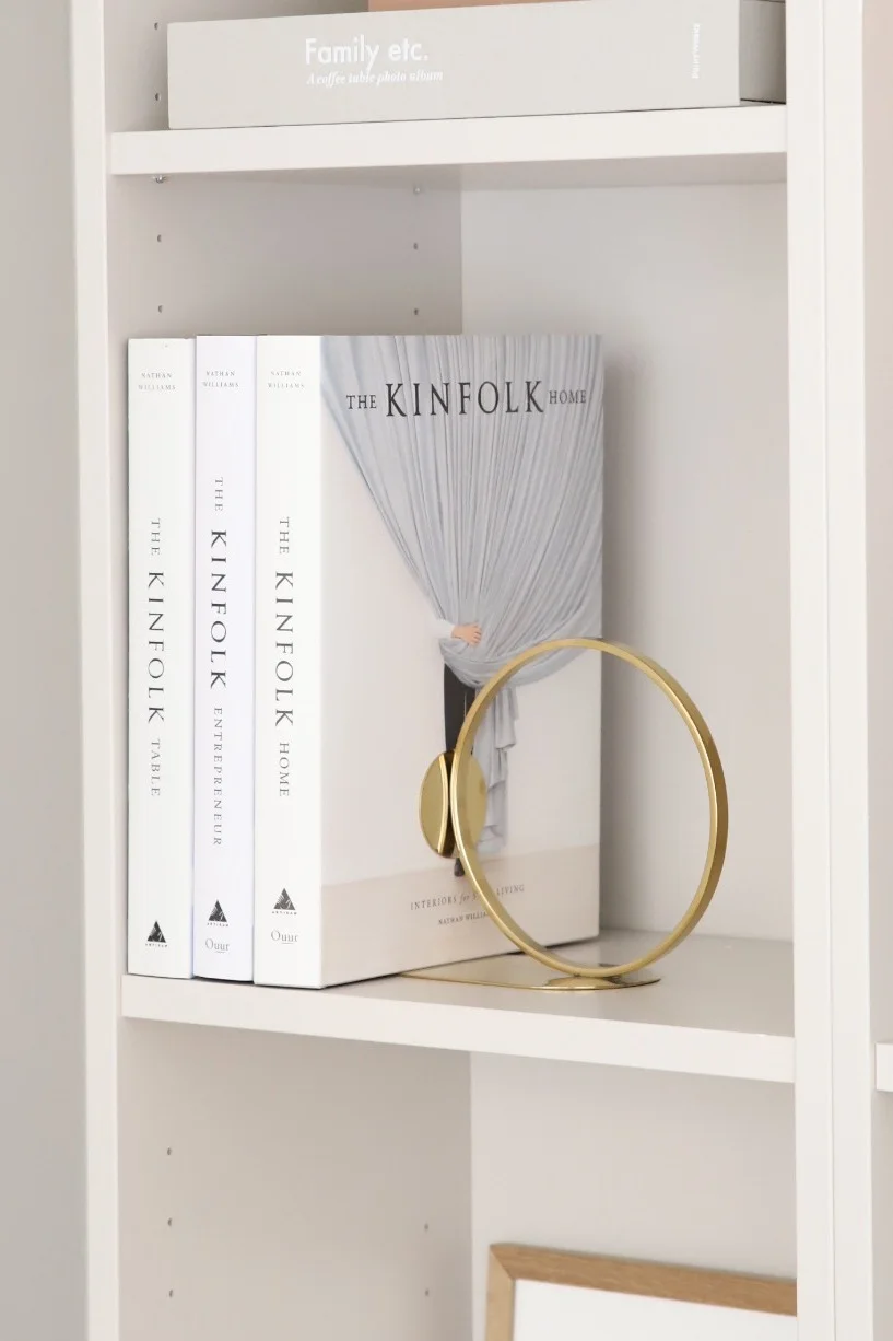 Wie wäre es mit einem guten Buch als Geschenk zum Muttertag? Verschenken Sie, passend dazu, gleich noch eine passende Buchstütze, wie den goldenen Book Ring von Cooee Design, der hier in einem Regal steht.