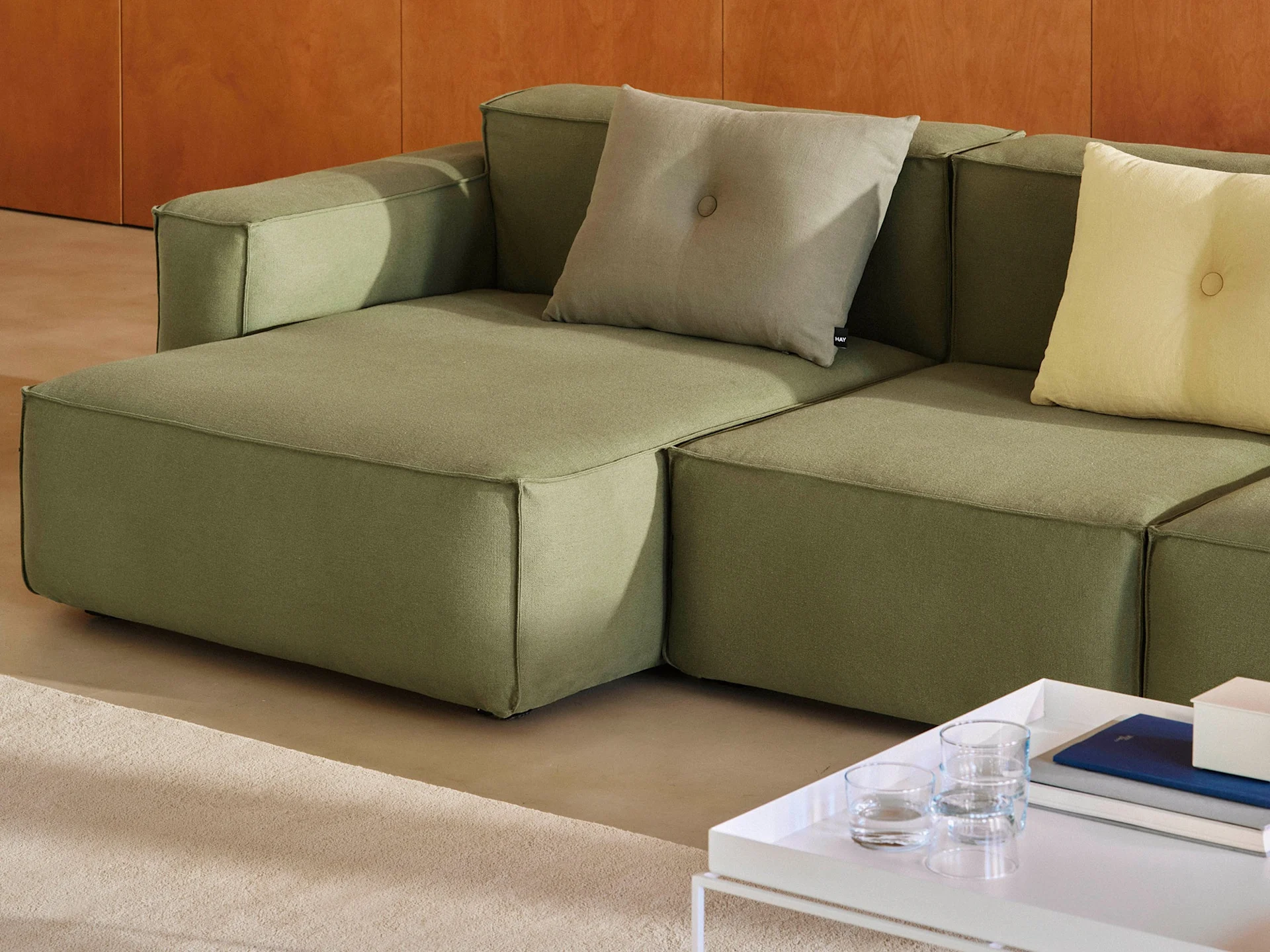 Ein modulares olivgrünes Sofa mit hellgrauen und gelben Zierkissen, neben einem weißen Couchtisch mit Büchern.