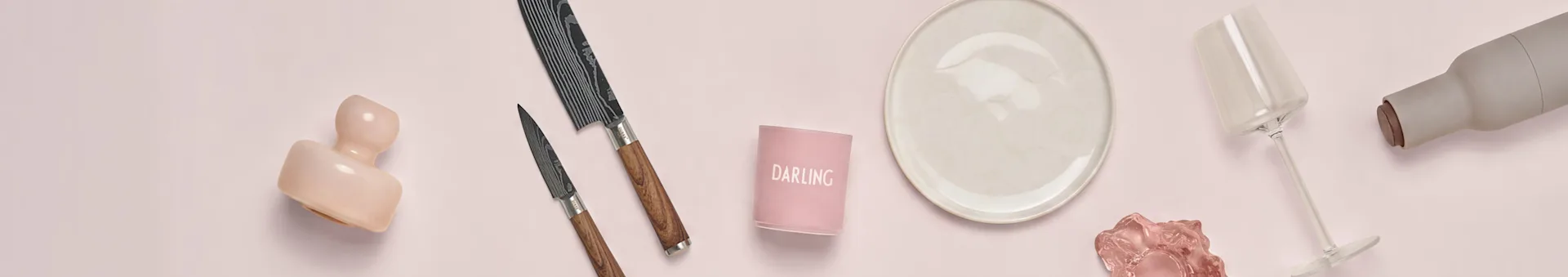 Deko auf Rosa: rosa Vase, gemusterte Messer, 'DARLING' Kerzenhalter, beiger Teller, Weinglas, graue Flasche.