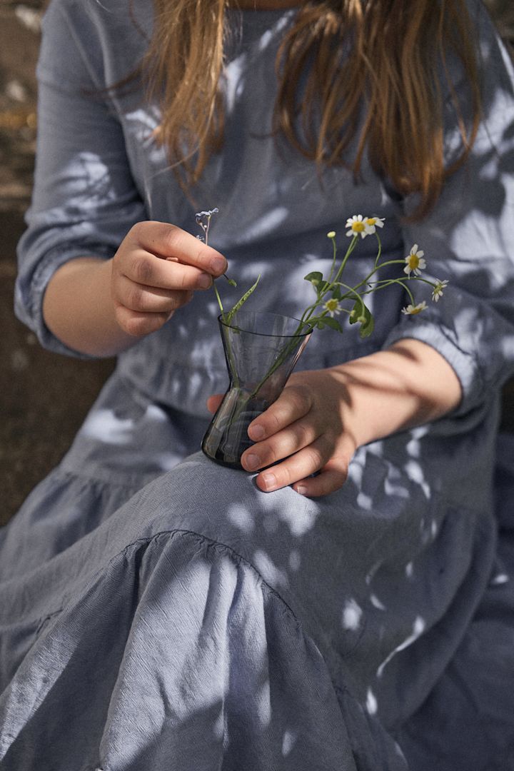 Mittsommer 2025: Eine Mittsommer-Tradition in Schweden besteht darin, Blumen zu pflücken. Hier sehen Sie ein Mädchen in blauem Kleid mit einer Midsummer-Vase mit Blumen auf dem Schoß.