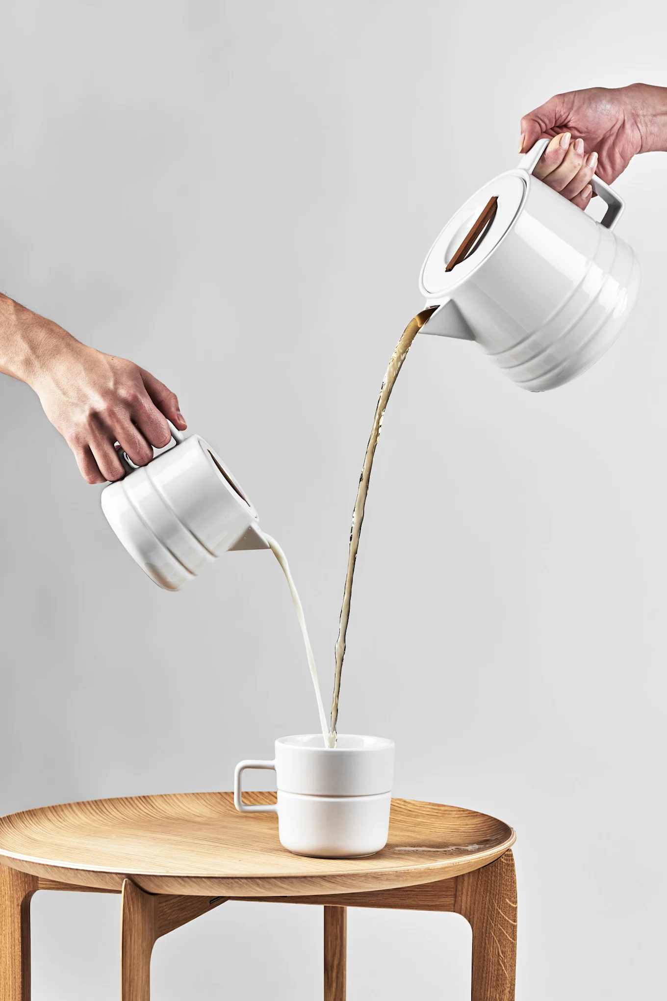 Große Kaffeetassen: Die weiße Lines-Tasse von NJRD steht auf einem Beistelltisch, während von weiter oben Kaffee und Milch aus den entsprechenden Kannen eingegossen werden.