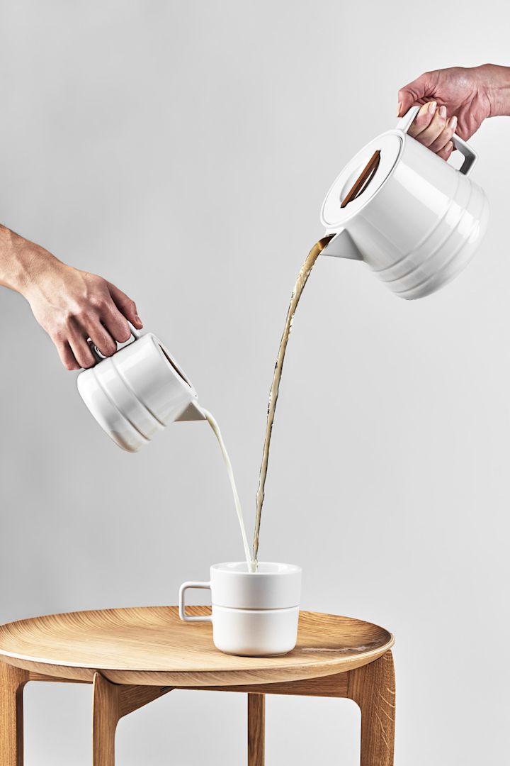 Große Kaffeetassen: Die weiße Lines-Tasse von NJRD steht auf einem Beistelltisch, während von weiter oben Kaffee und Milch aus den entsprechenden Kannen eingegossen werden.