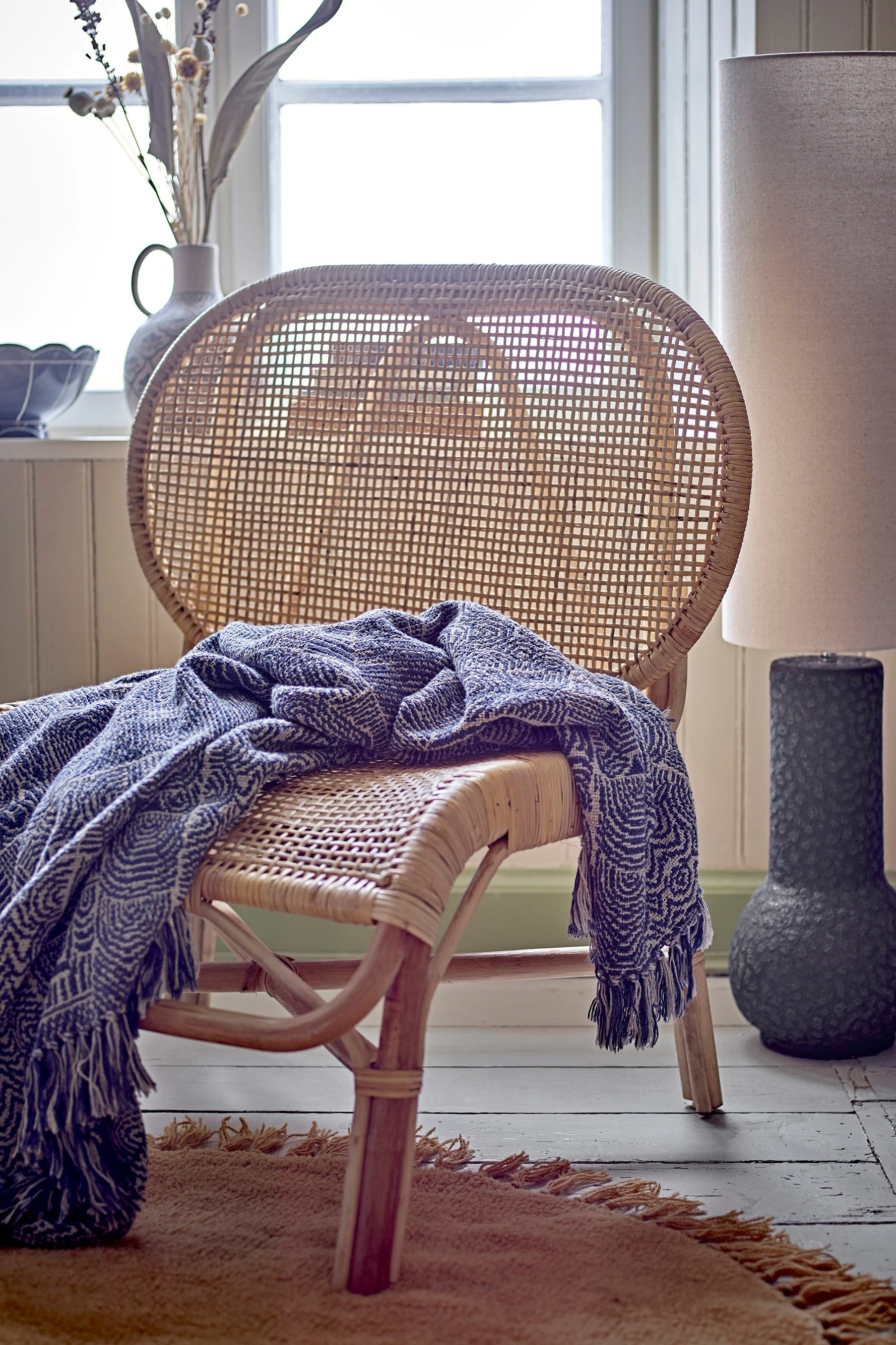 Boho Deko: Die gemusterte Bresso Decke von Bloomingville auf einem Rattan-Sessel.